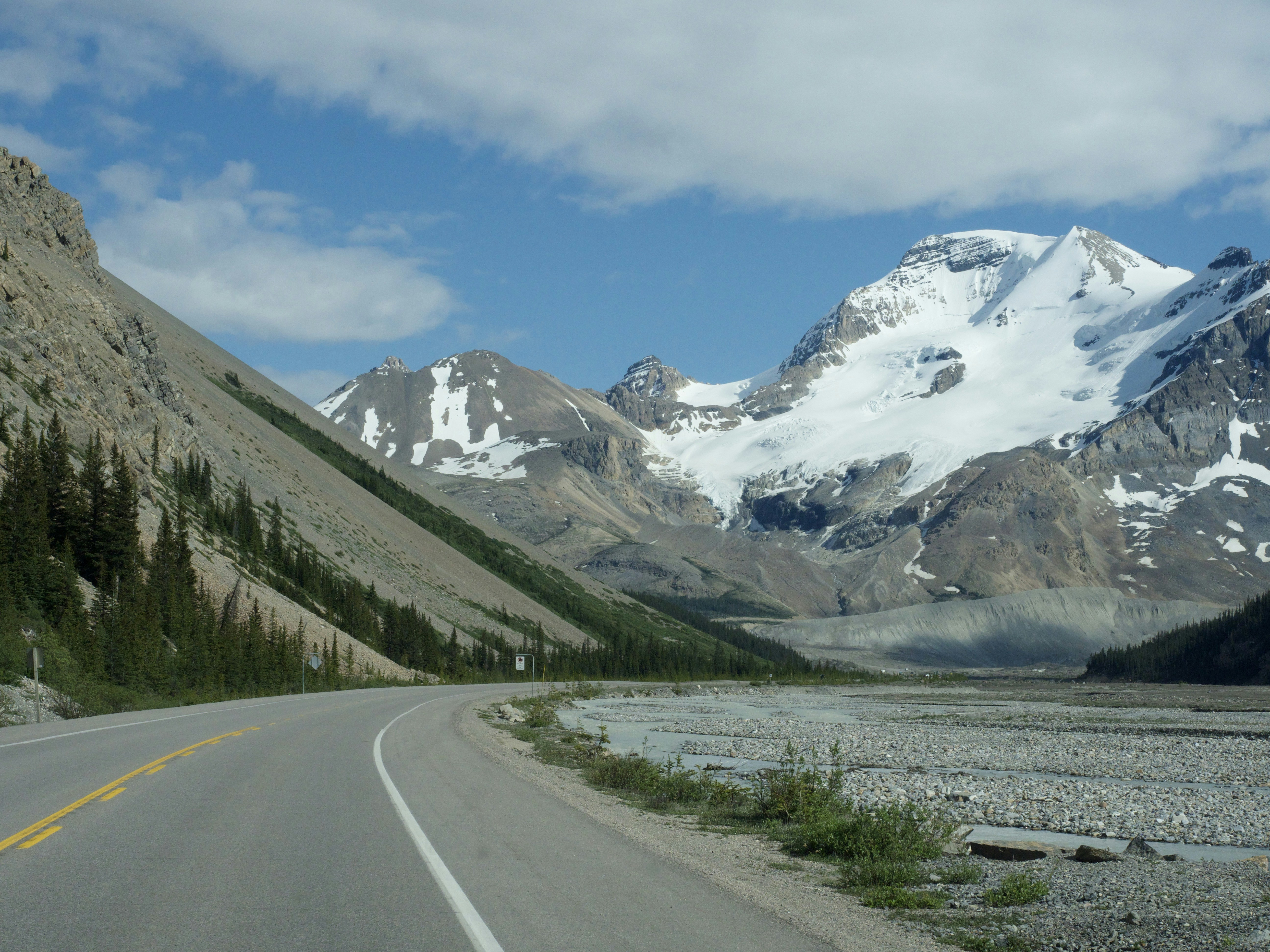 Strada di montagna panoramica con cime innevate e cielo azzurro
