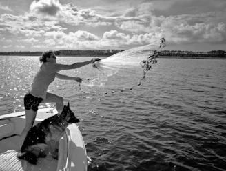 Man casting fishing net from boat with dog