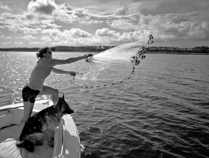 Man casting fishing net from boat with dog