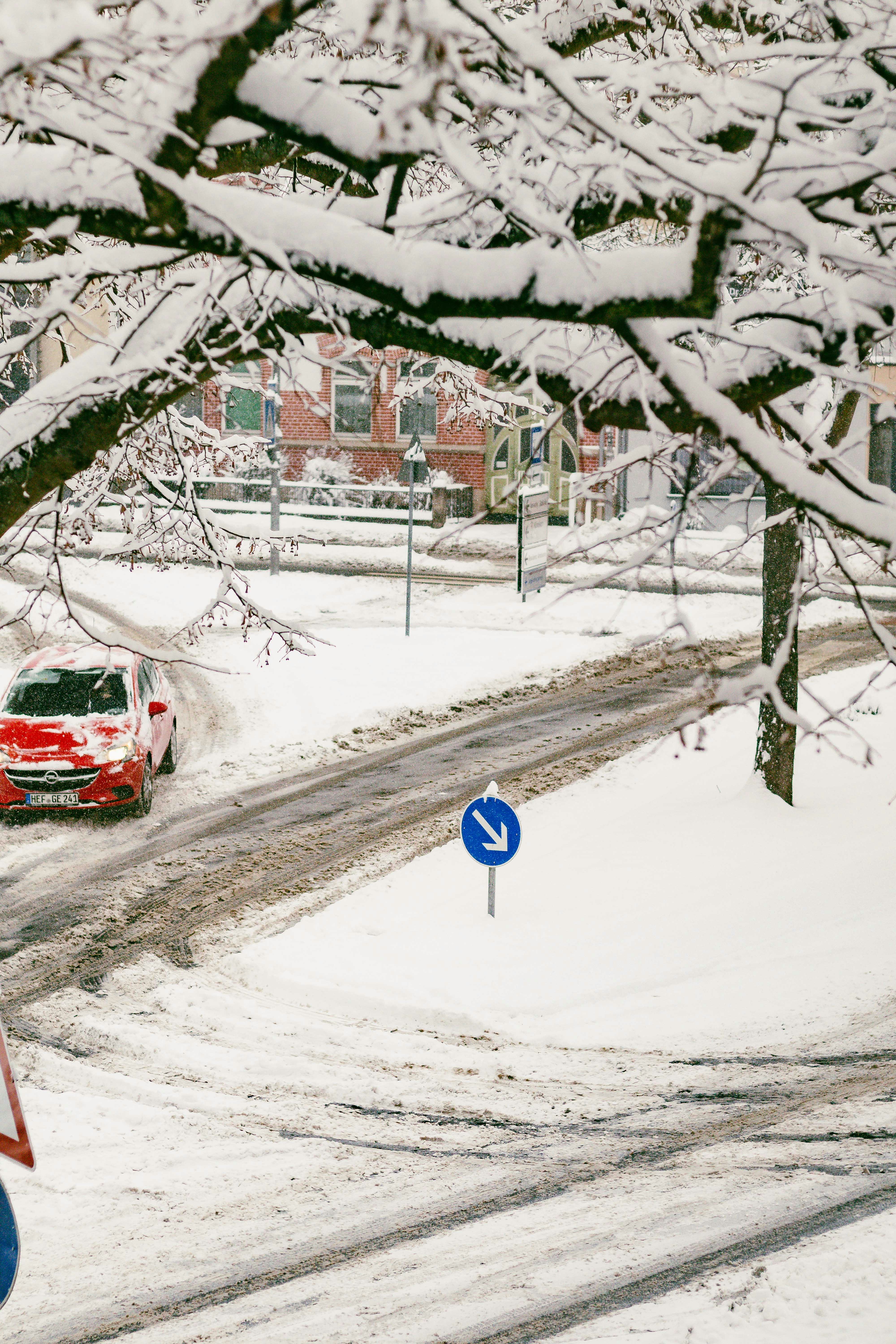 A red car drives on a snowy road with trees.