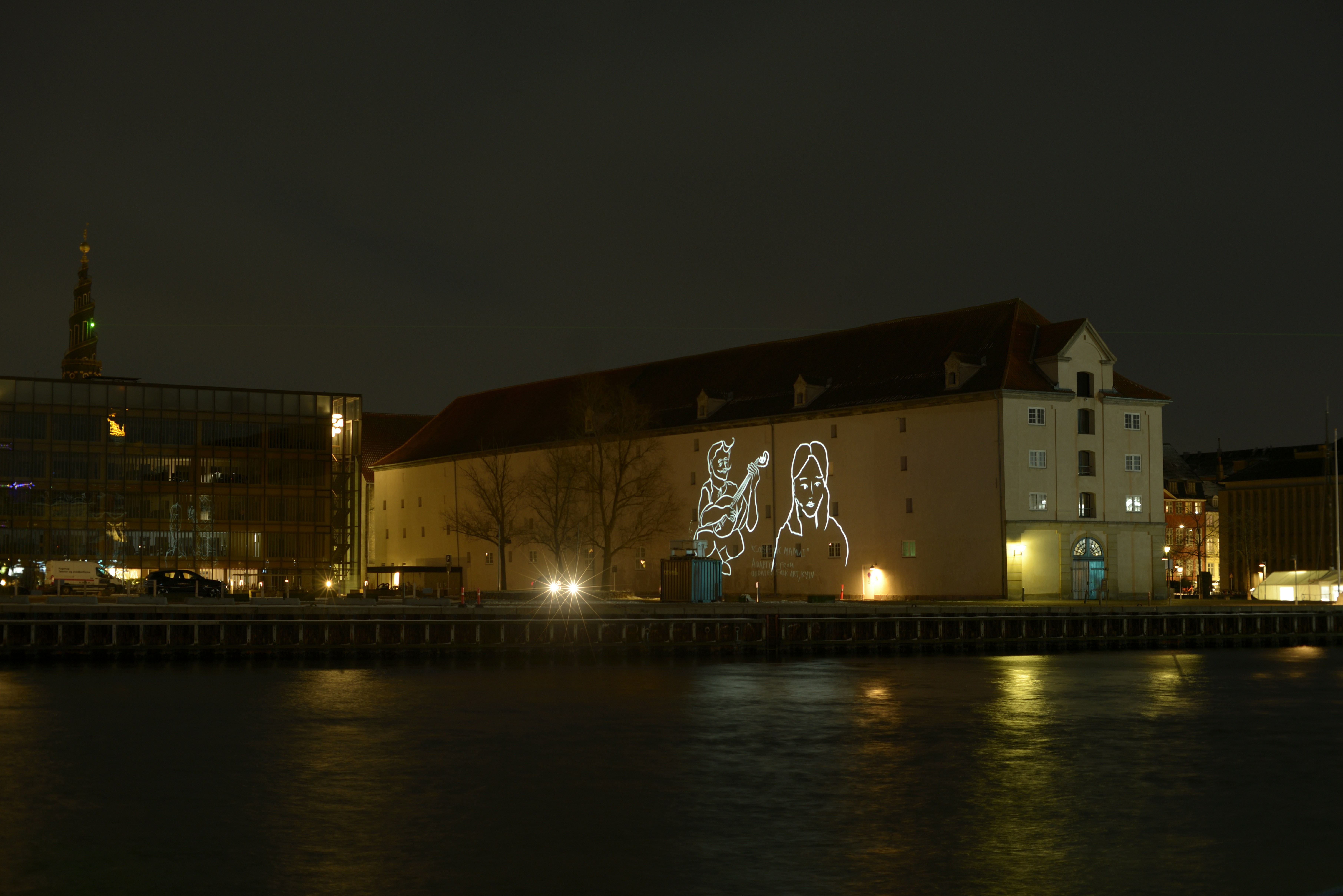 Building illuminated with vivid colorful light projections at night by water