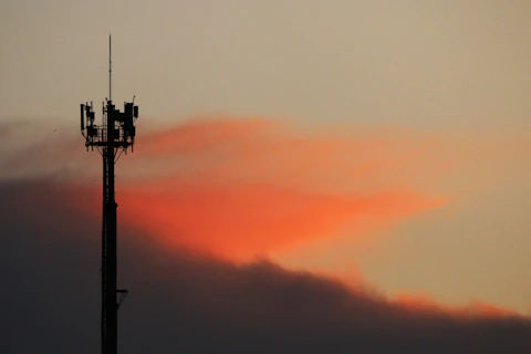 Cell tower silhouetted against a sunset sky