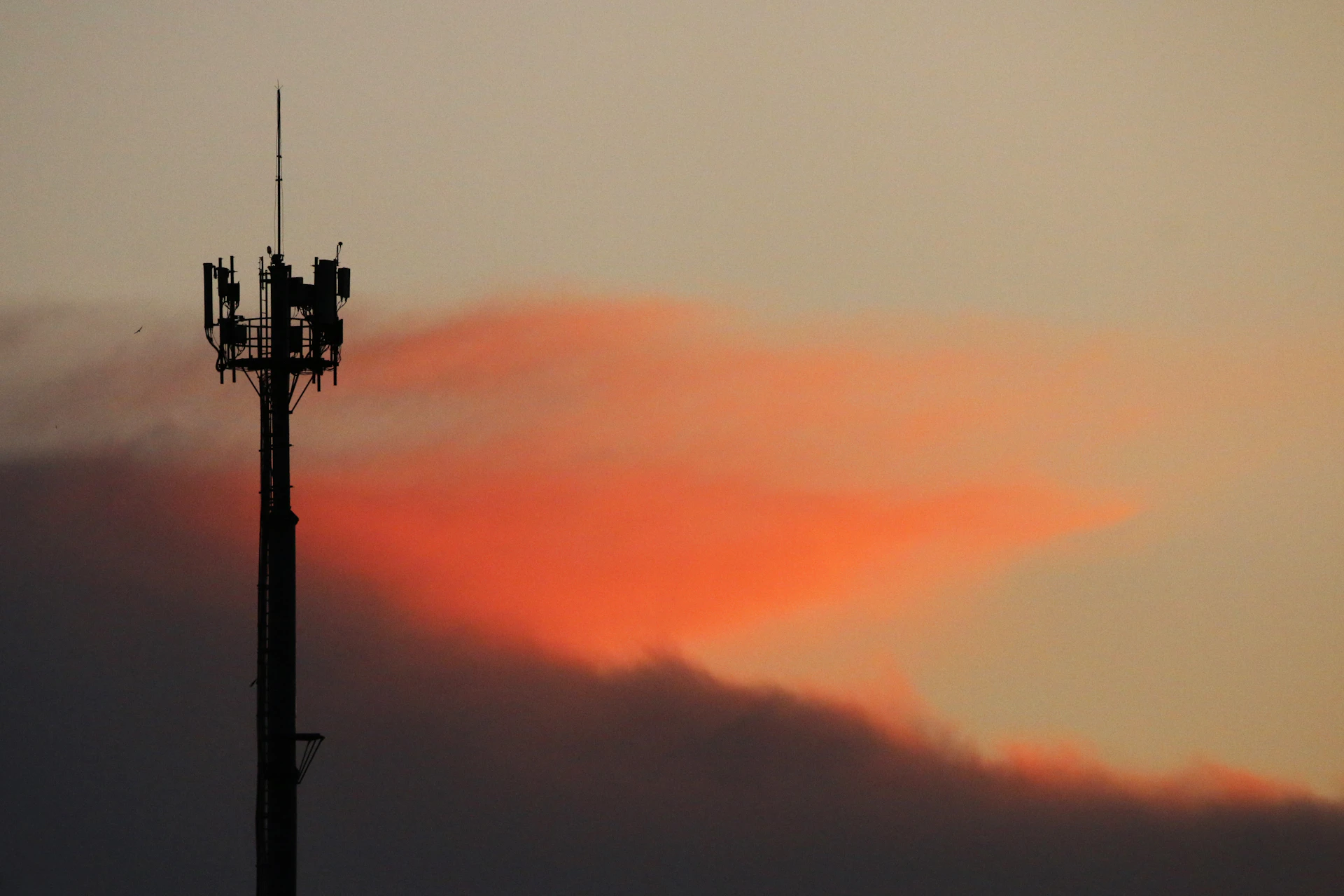 Cell tower silhouetted against a sunset sky