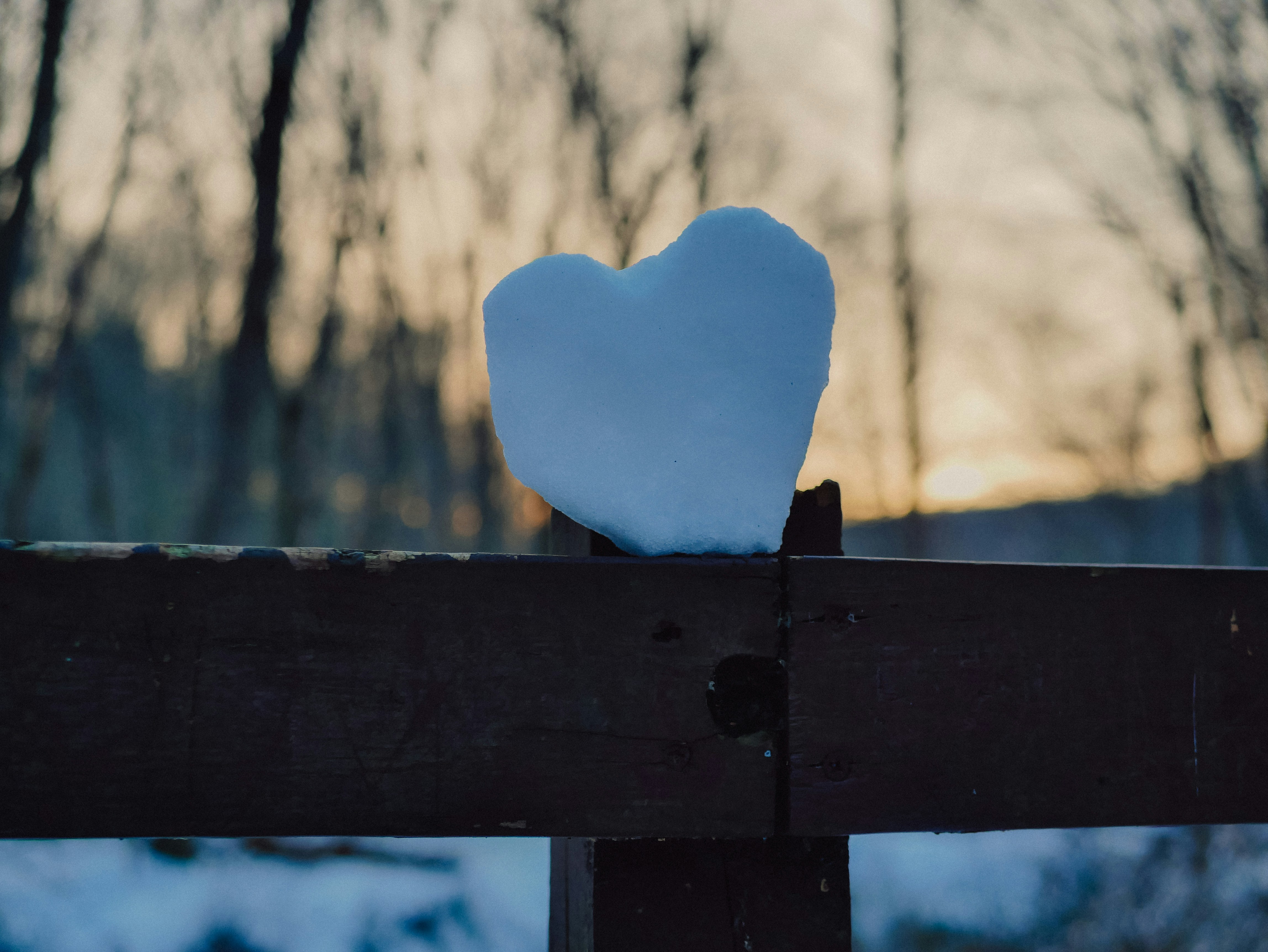 Heart-shaped snowball rests on a wooden fence.