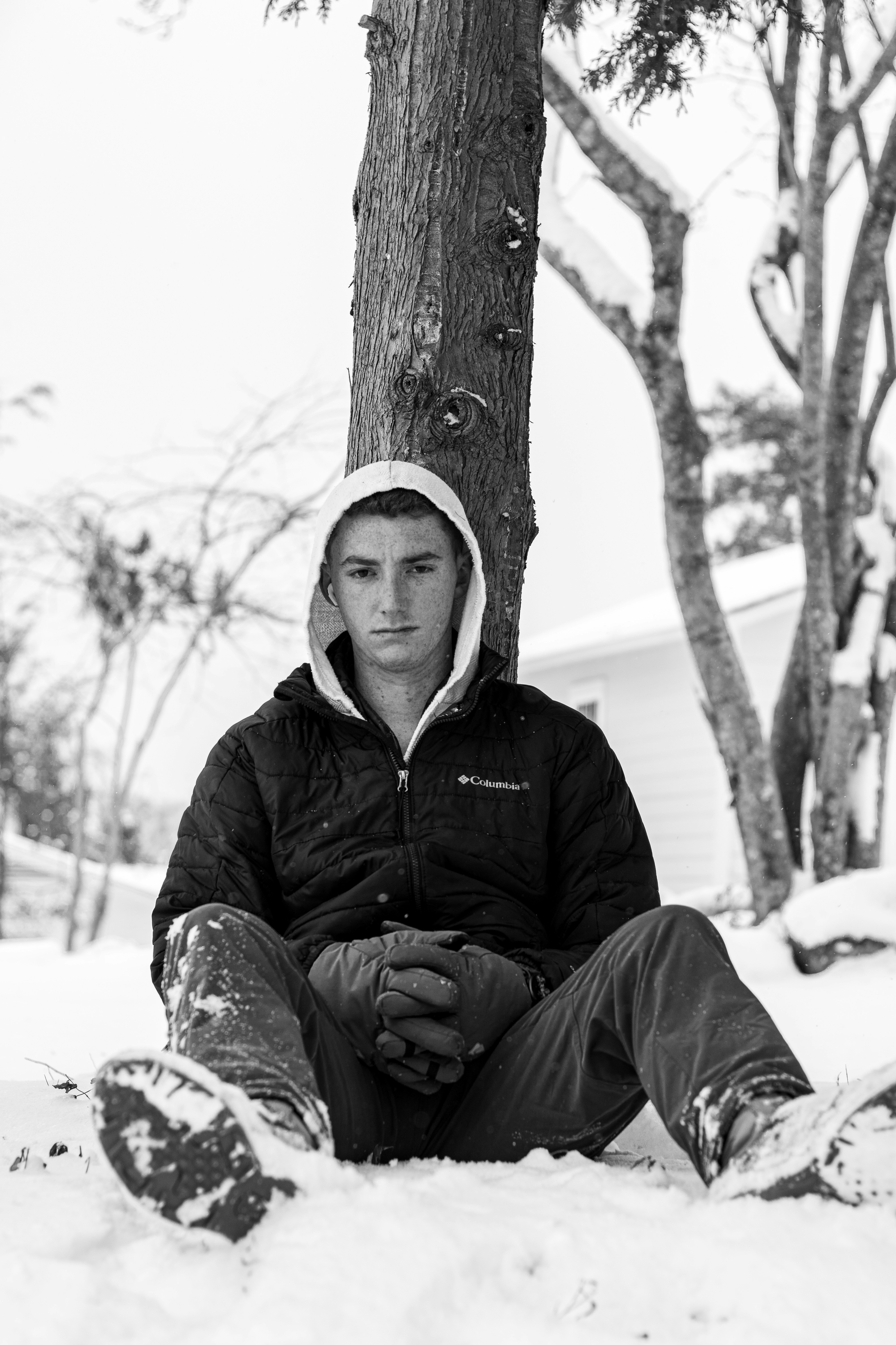 Young man sitting in snow under a tree