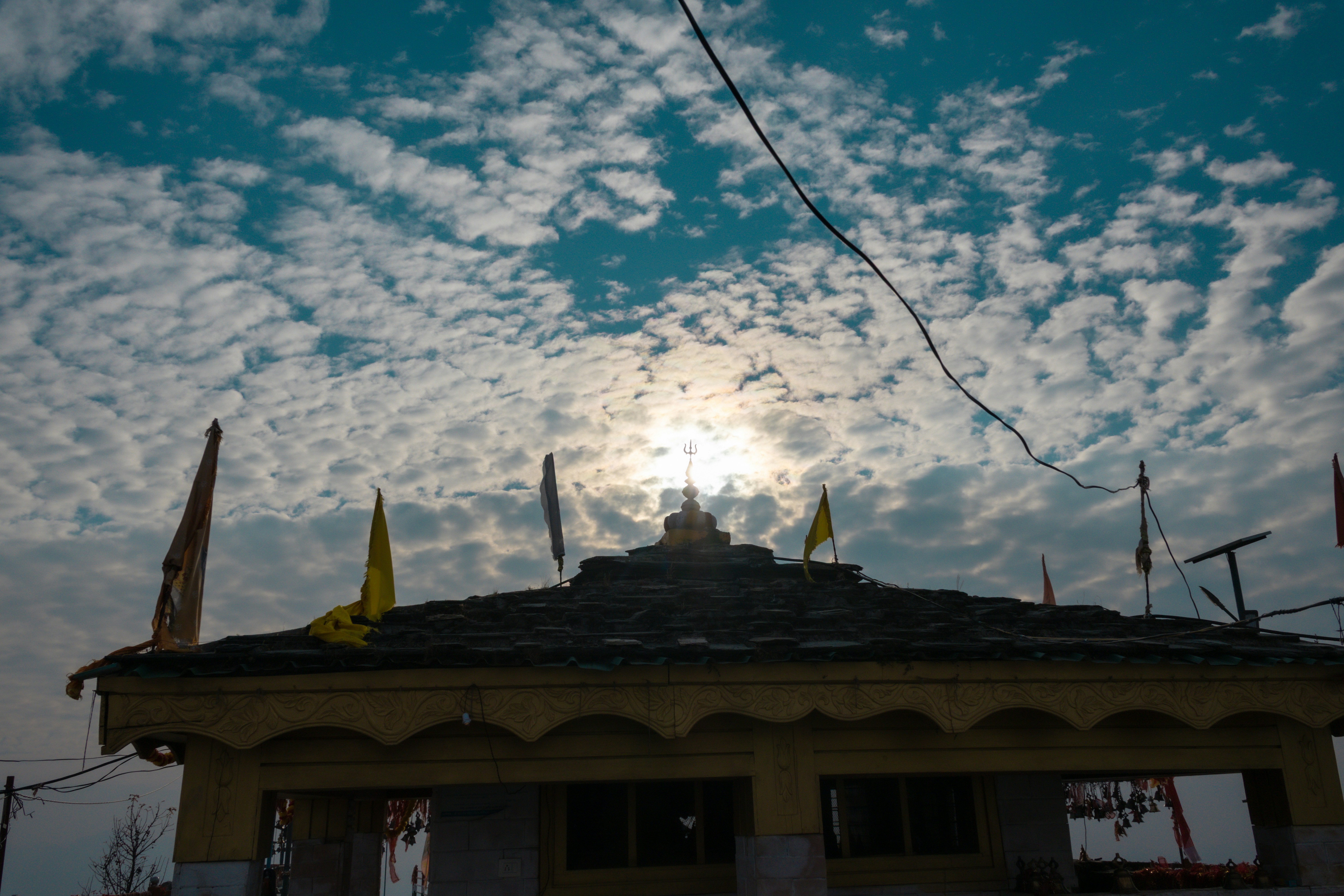 Sun behind temple roof with flags and clouds