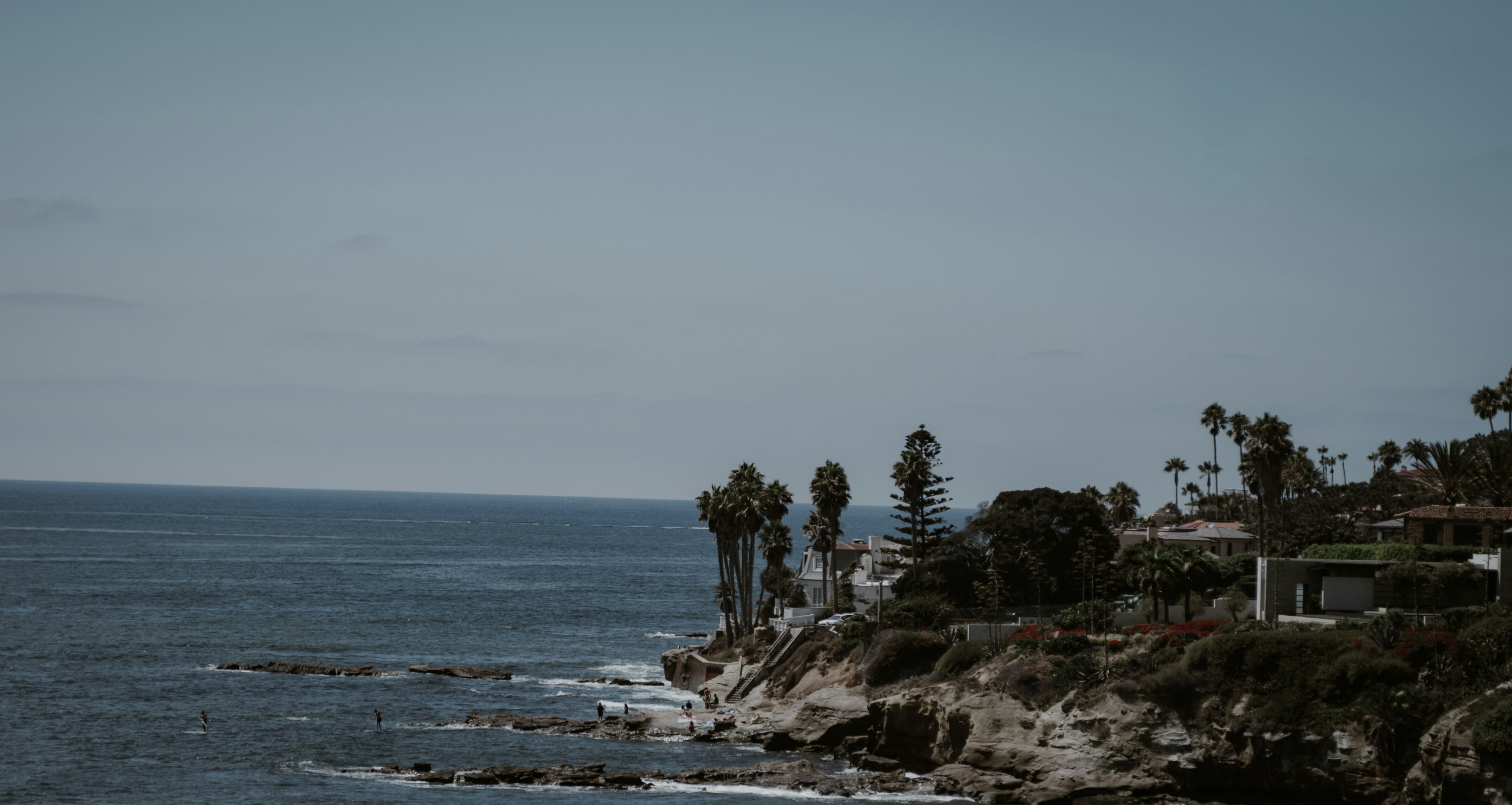 Ocean waves crash against a rocky coastline with palm trees.