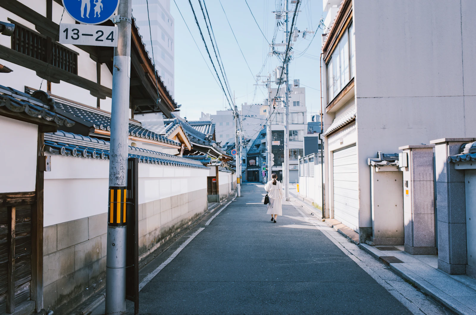 A traveler walking down a quiet street lined with traditional and modern buildings in Kyoto