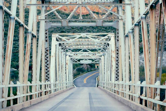 A weathered metal bridge crosses a winding road.