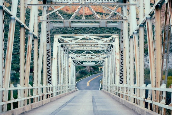 A weathered metal bridge crosses a winding road.