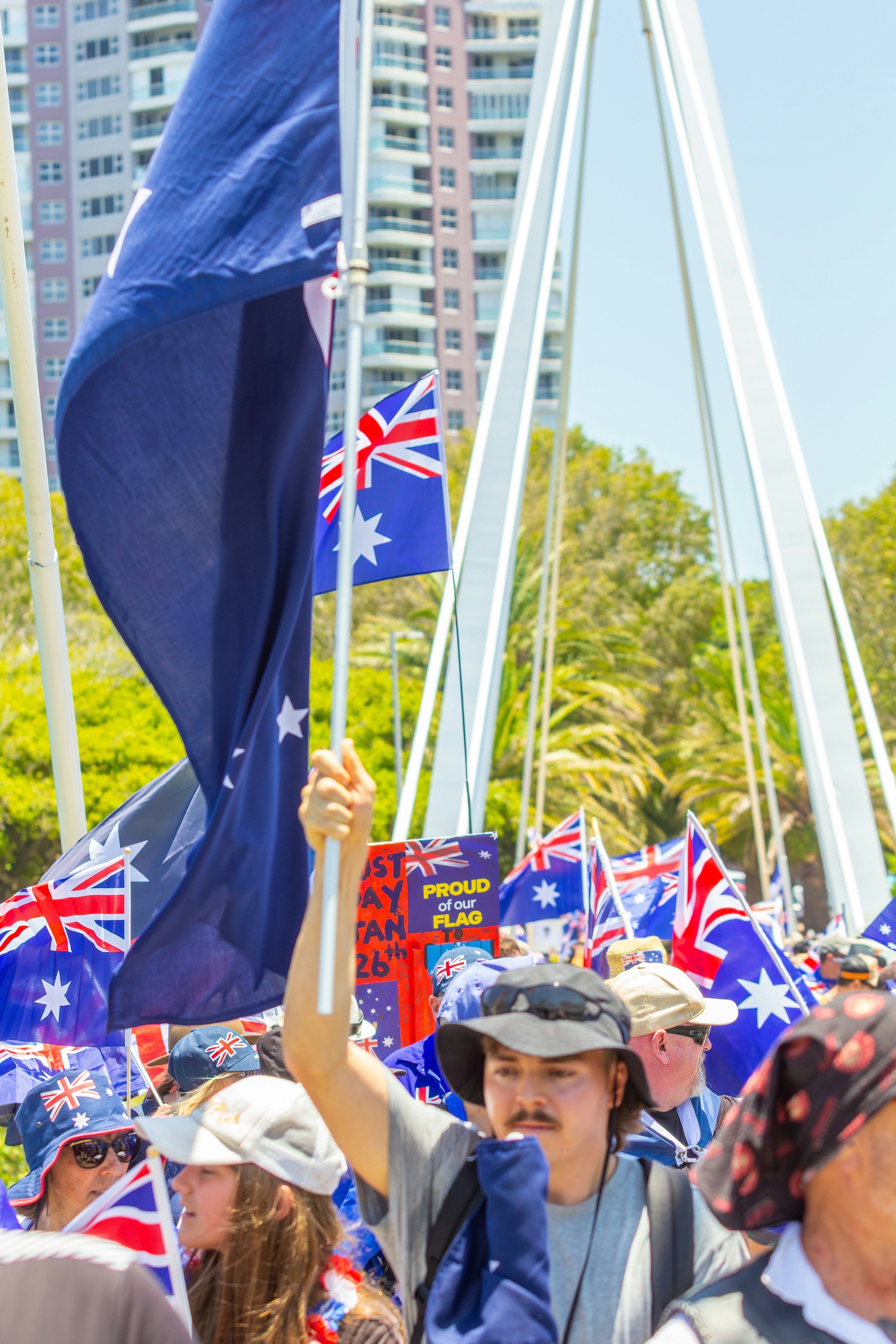 People wave australian flags at a sunny outdoor event.