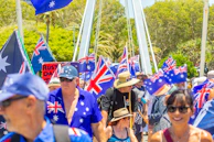 Crowd of people waving australian flags during a sunny day.