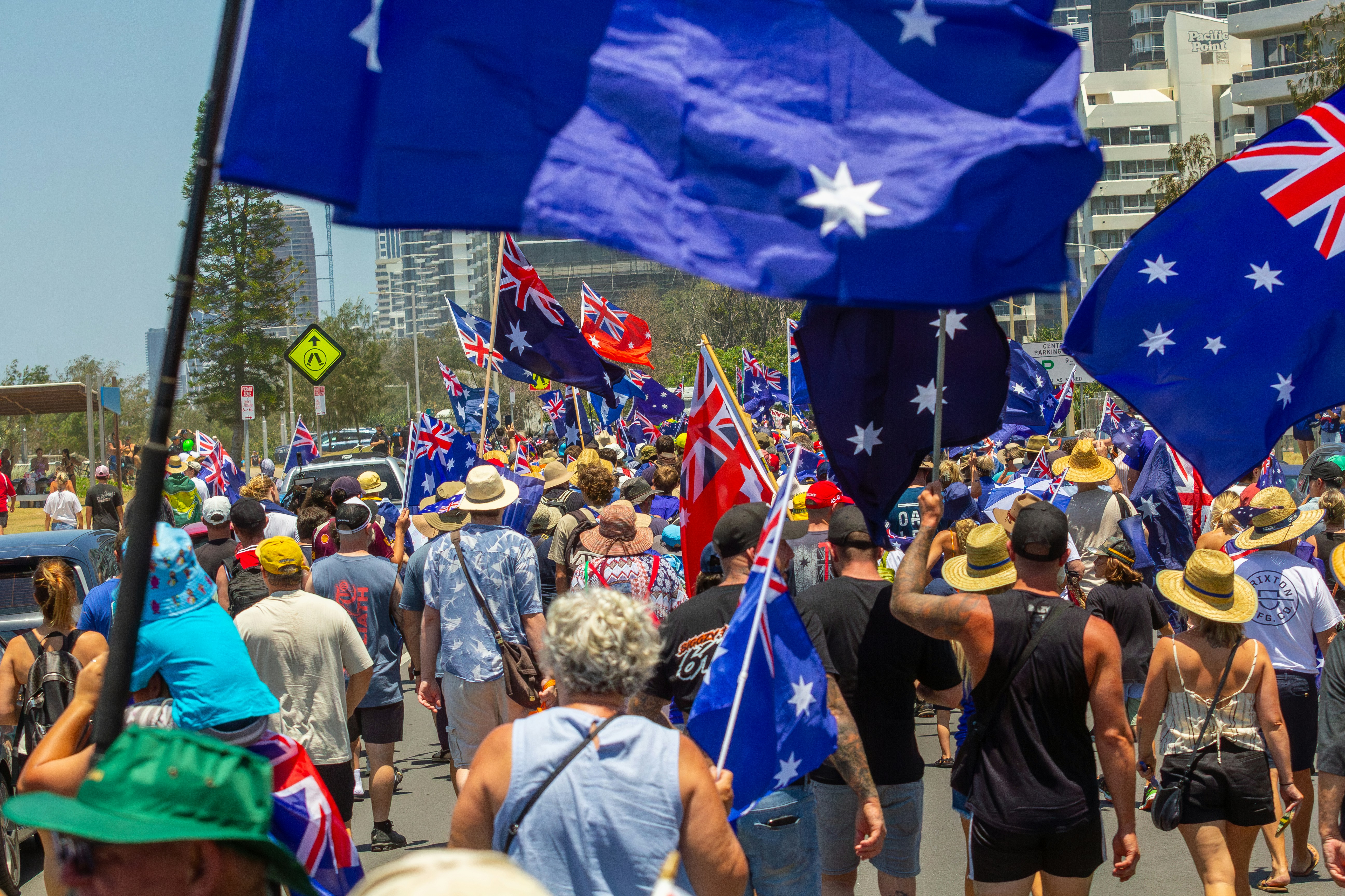 Crowd of people waving australian flags during a sunny day.