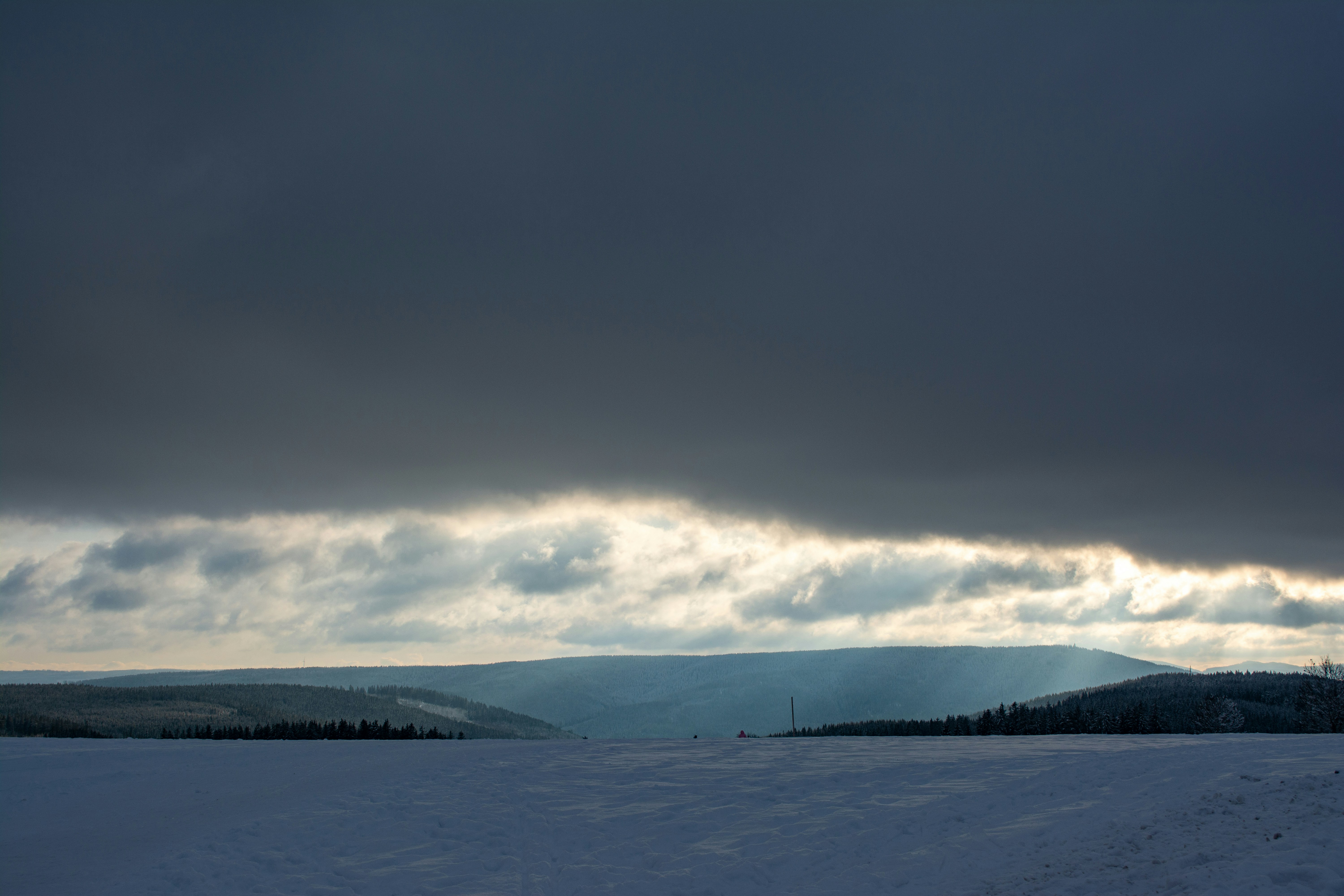 A breathtaking winter landscape unfolds beneath a heavy sky, where a sliver of light breaks through dense clouds—reminding us that even the darkest storms fade. ❄️