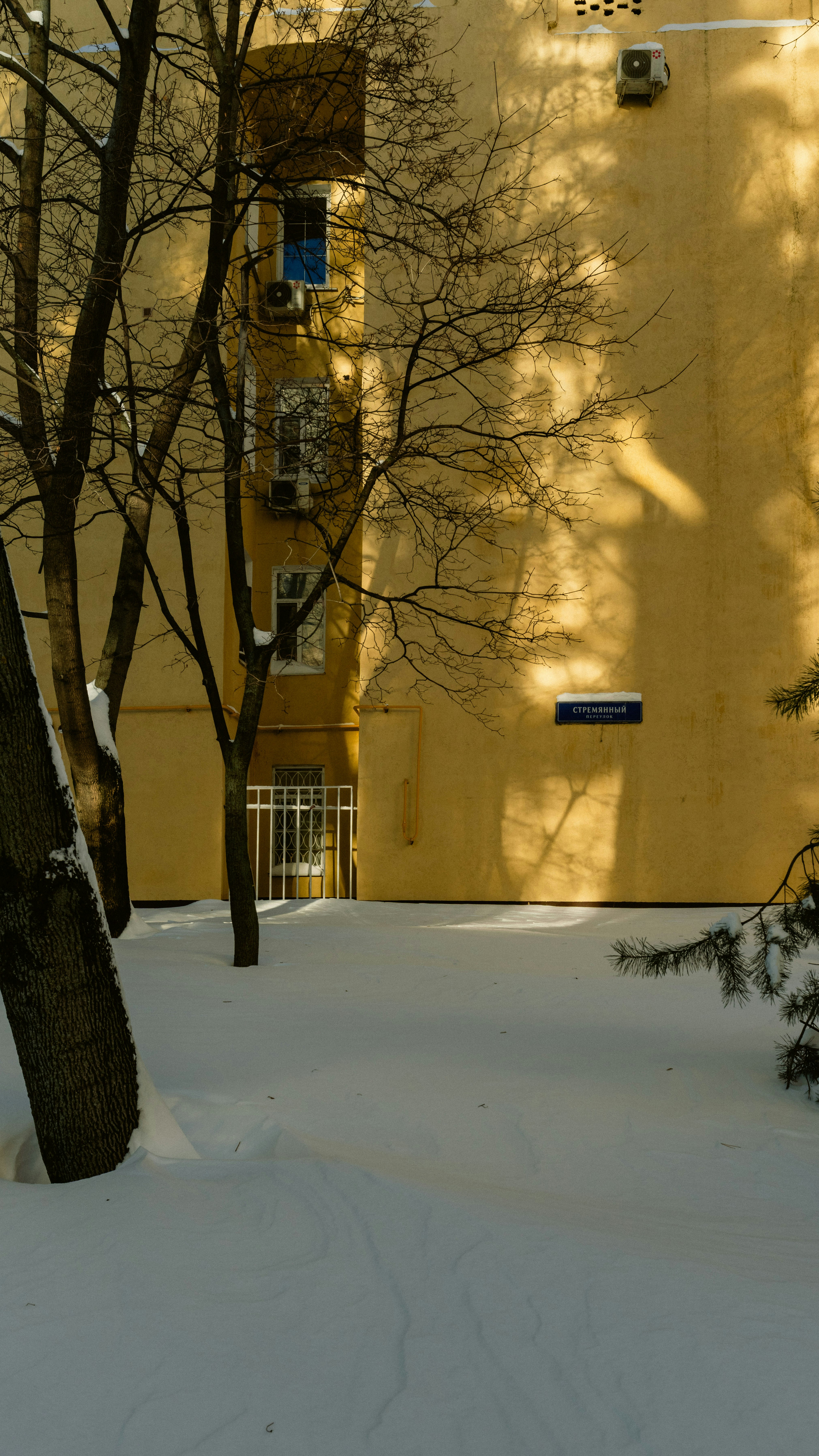 Yellow building facade with snow-covered ground and bare trees.