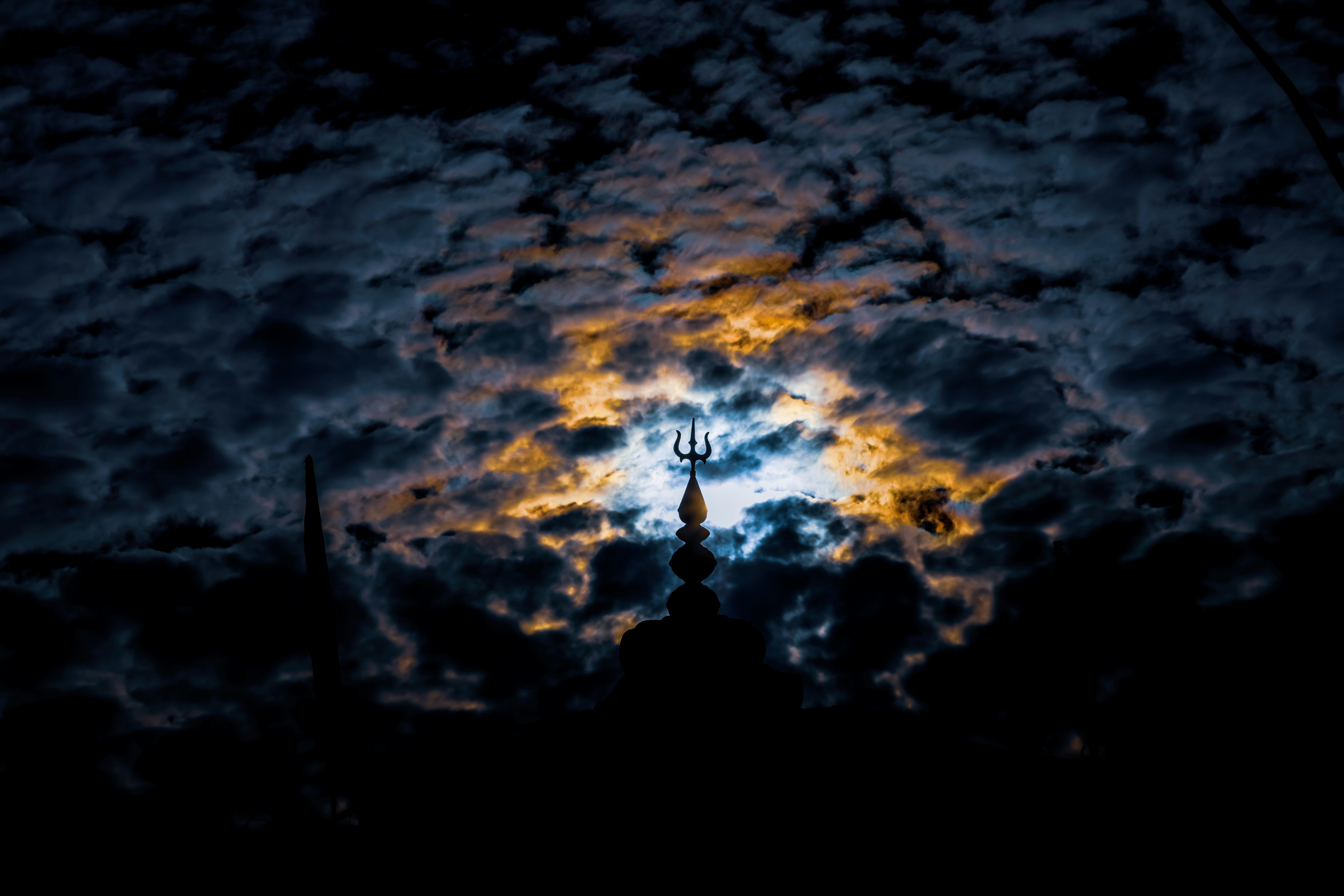 Moonlight shines through dark clouds over a silhouetted tower.