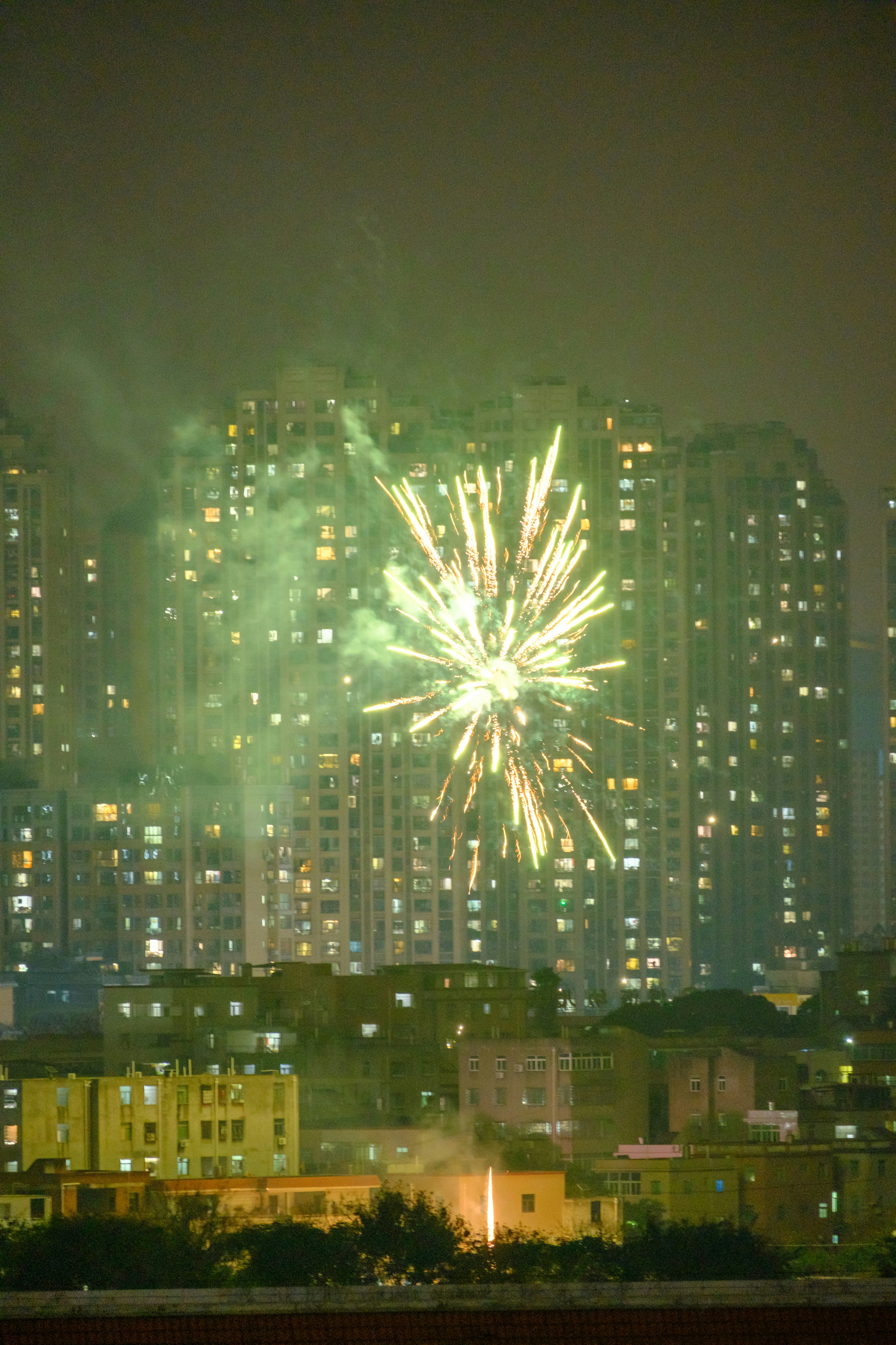 Green fireworks explode over a city skyline at night.