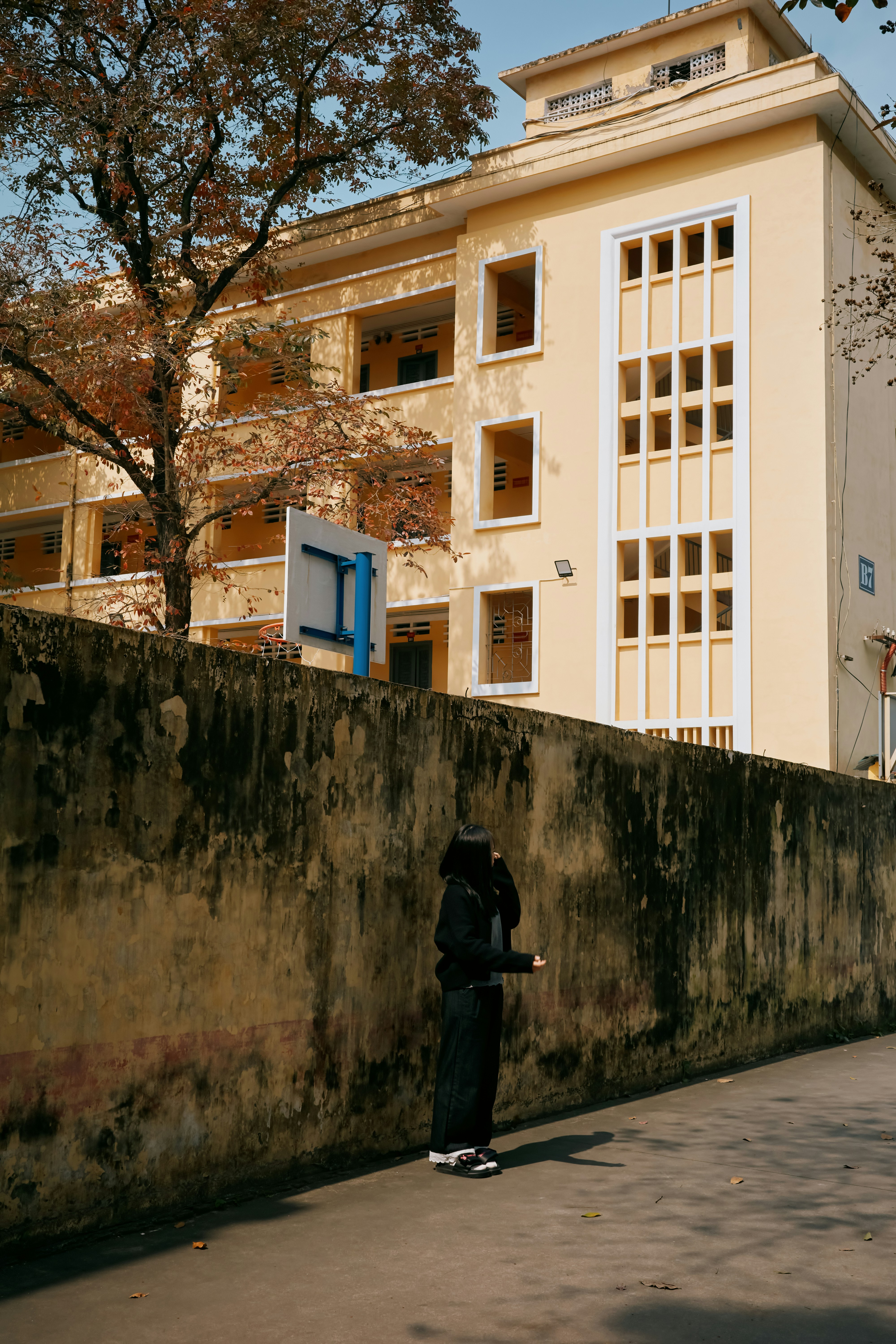 人物は風化した壁と黄色い建物の近くに立っている。