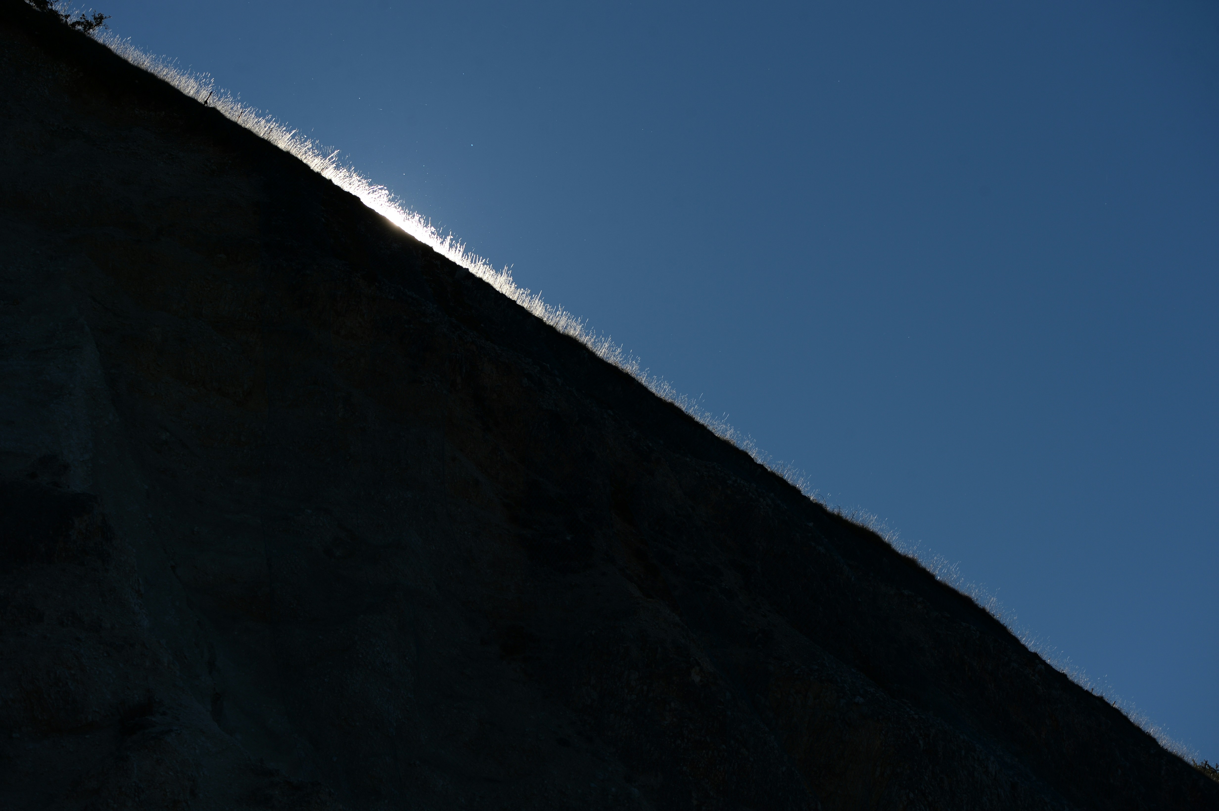 Sunlight glinting off a dark, grassy slope against blue sky