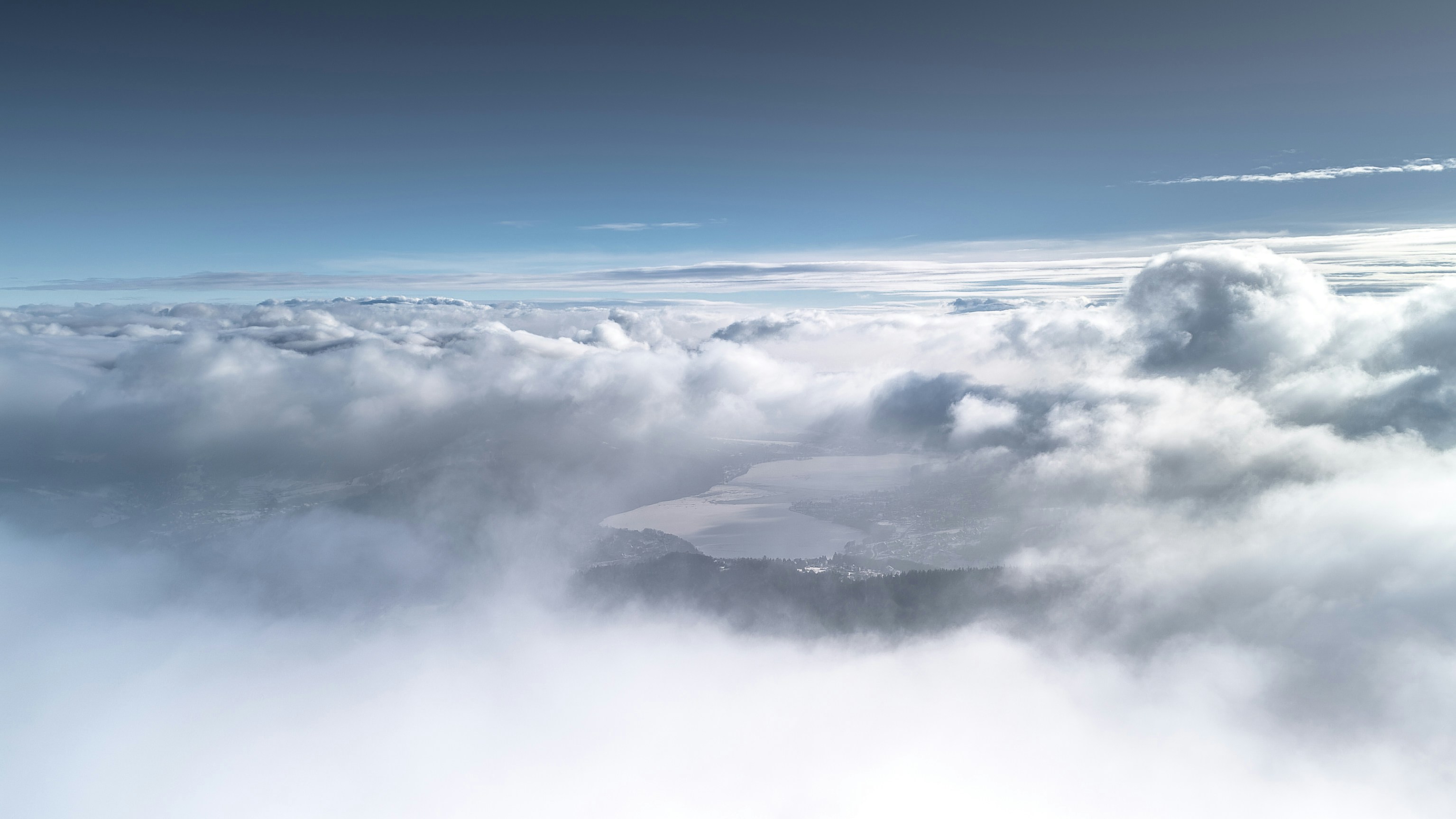 Des nuages blancs et duveteux recouvrent un paysage montagneux en contrebas.