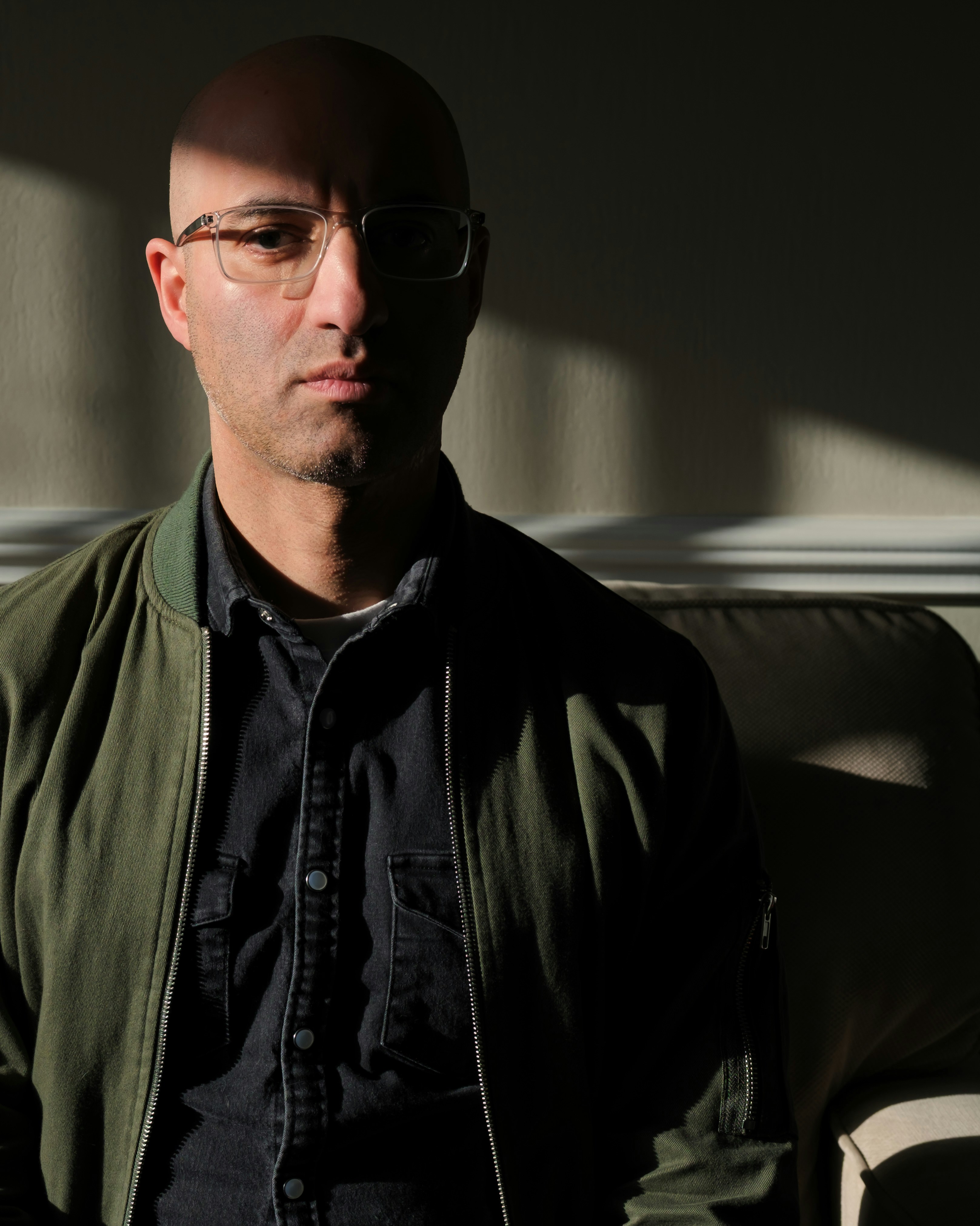 Bald man with glasses wearing a bomber jacket.