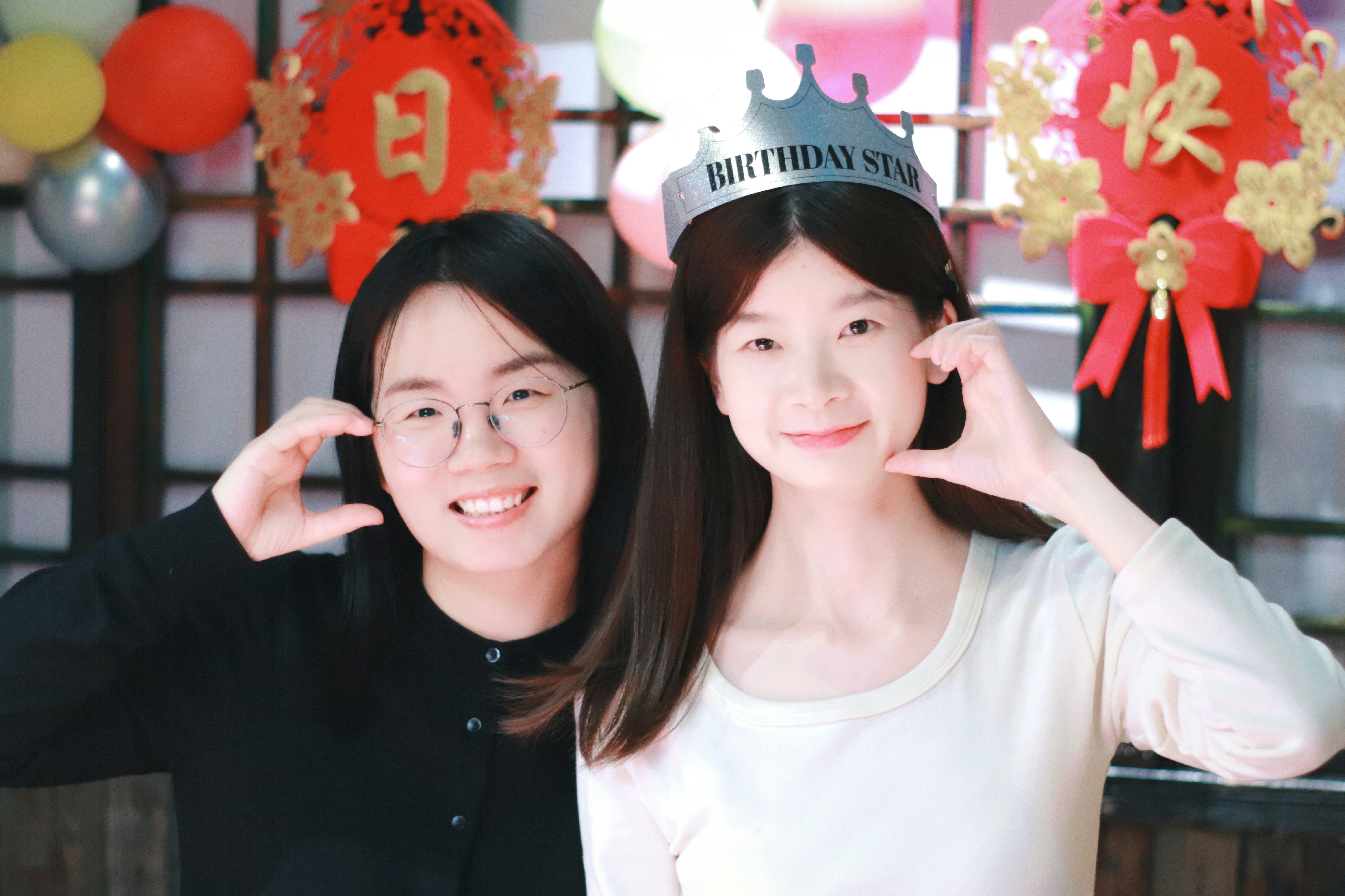 Two smiling young women making heart shapes with hands.