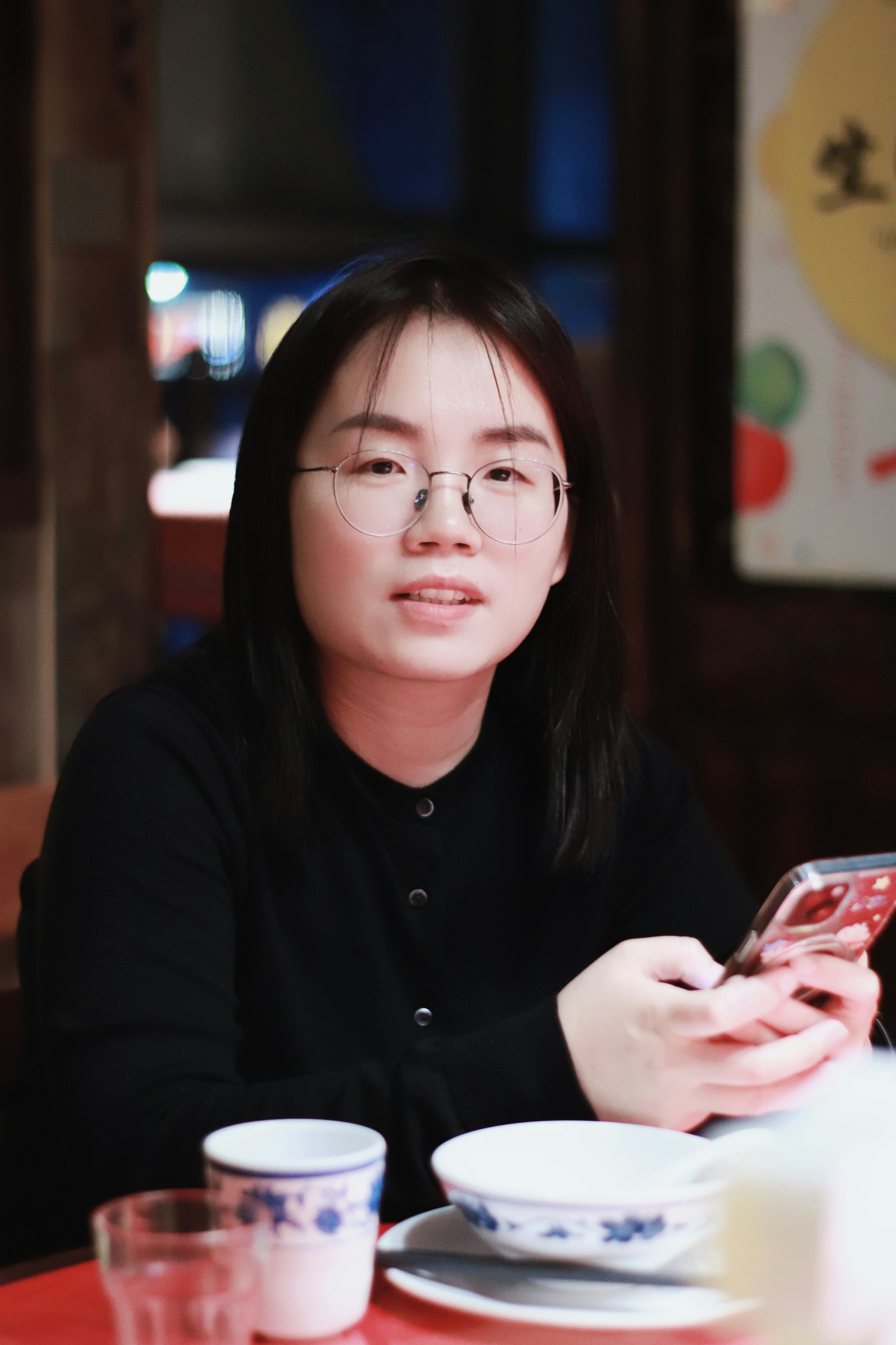 A young woman with glasses holding a smartphone.