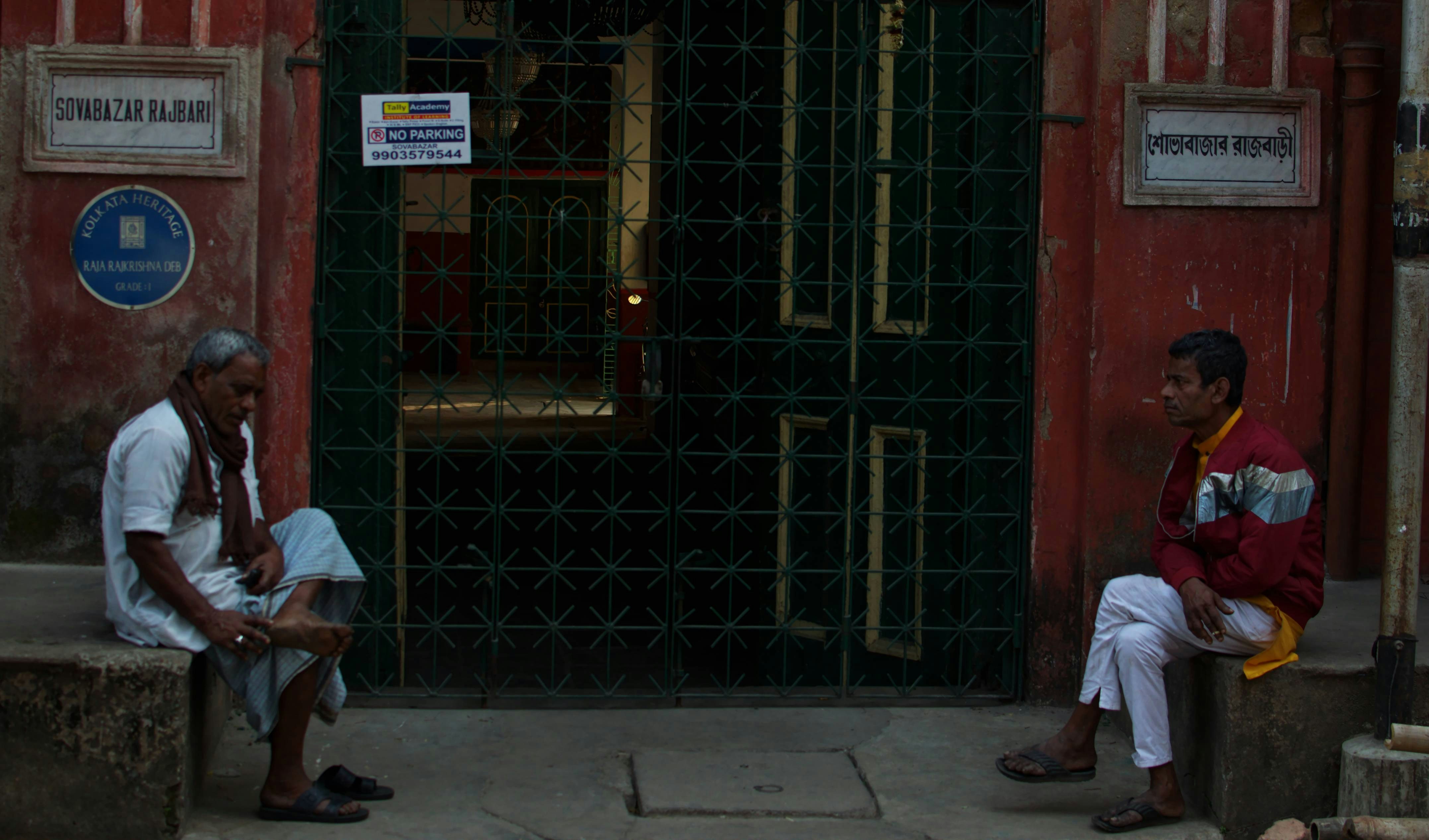 Two men sitting outside a building entrance.