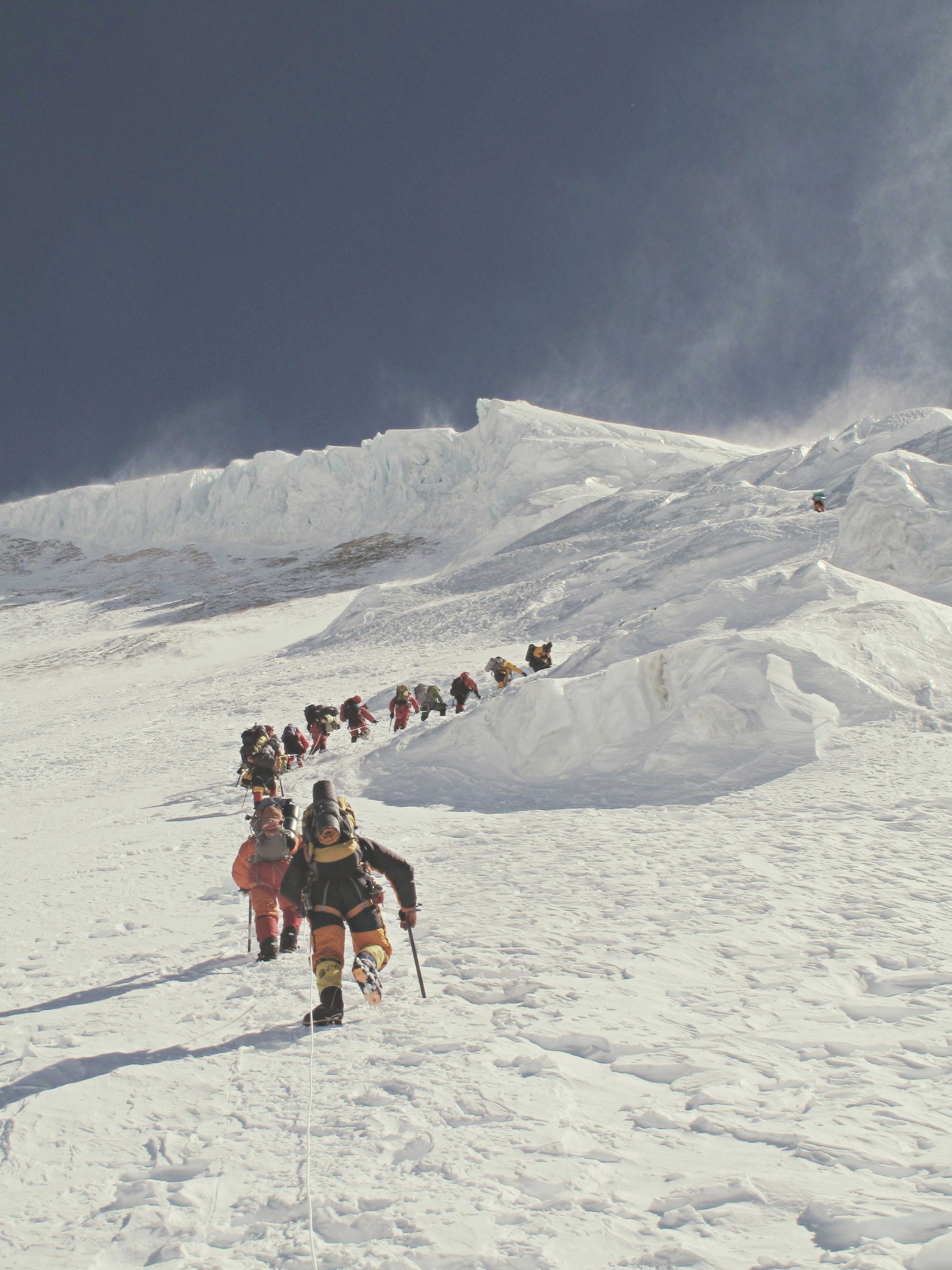 Climbers ascend a steep, snowy mountain slope