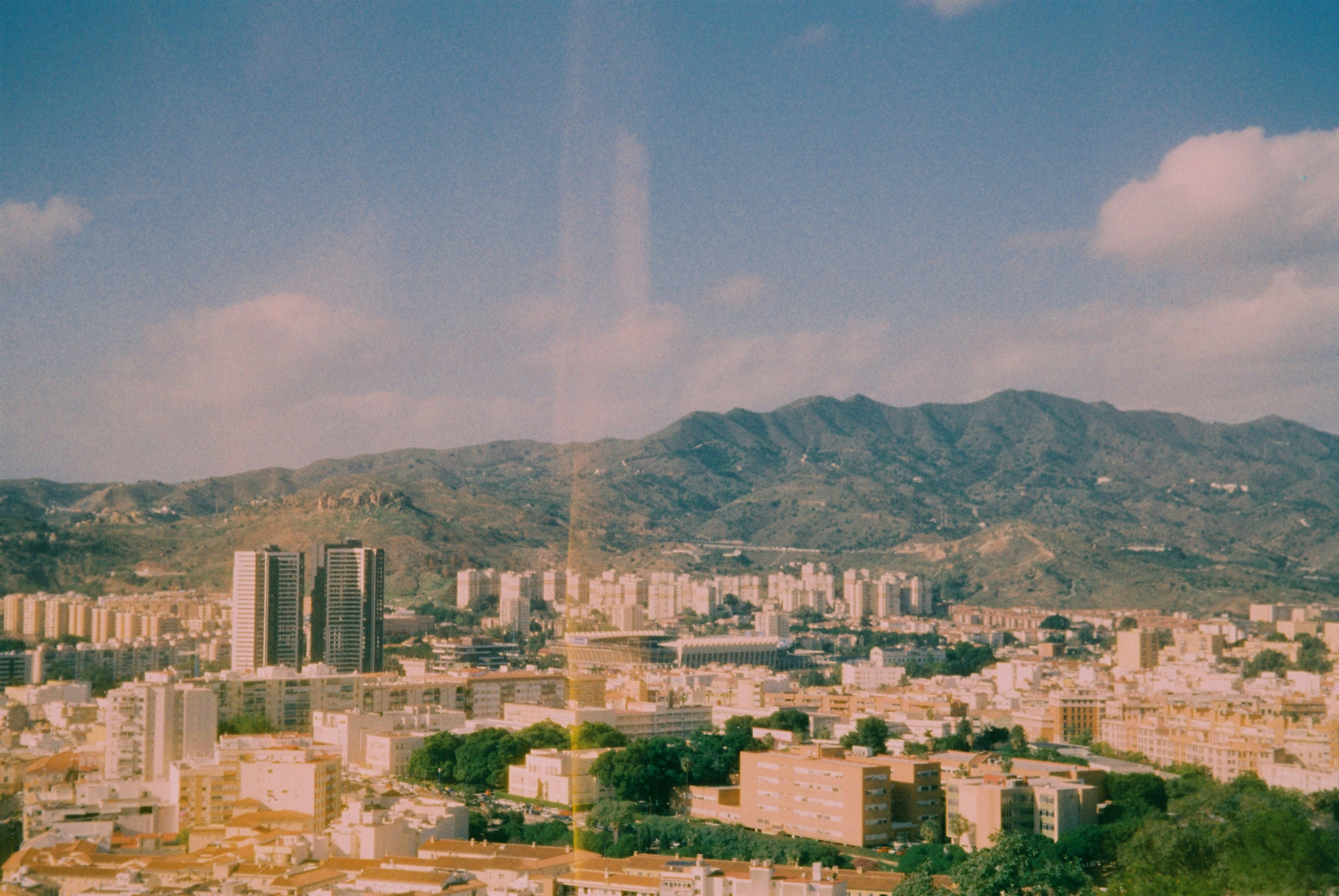 Cityscape with buildings and mountains under a clear sky.