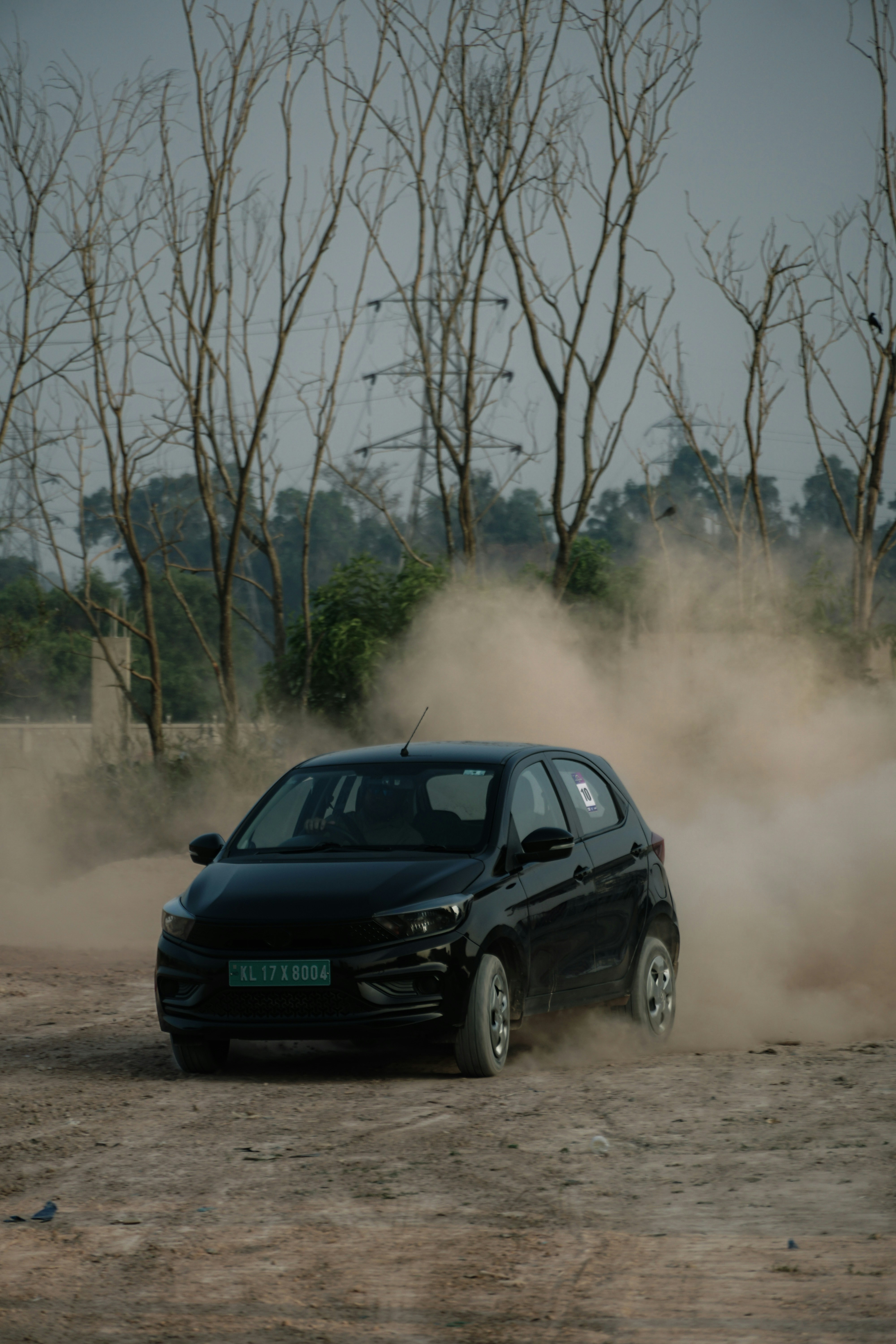 A black car driving through dust on a dirt road.