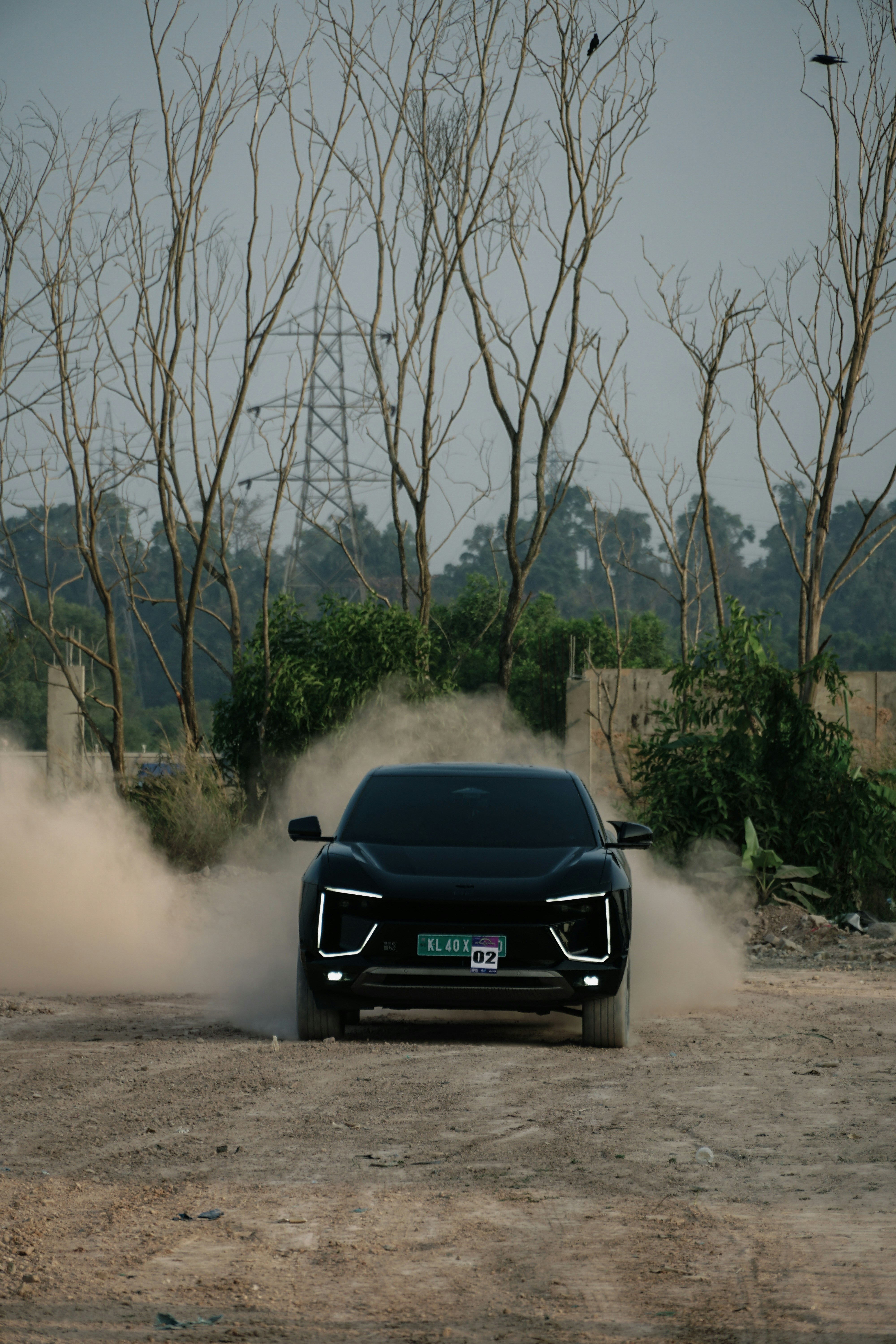 A black car kicks up dust on a dirt road.