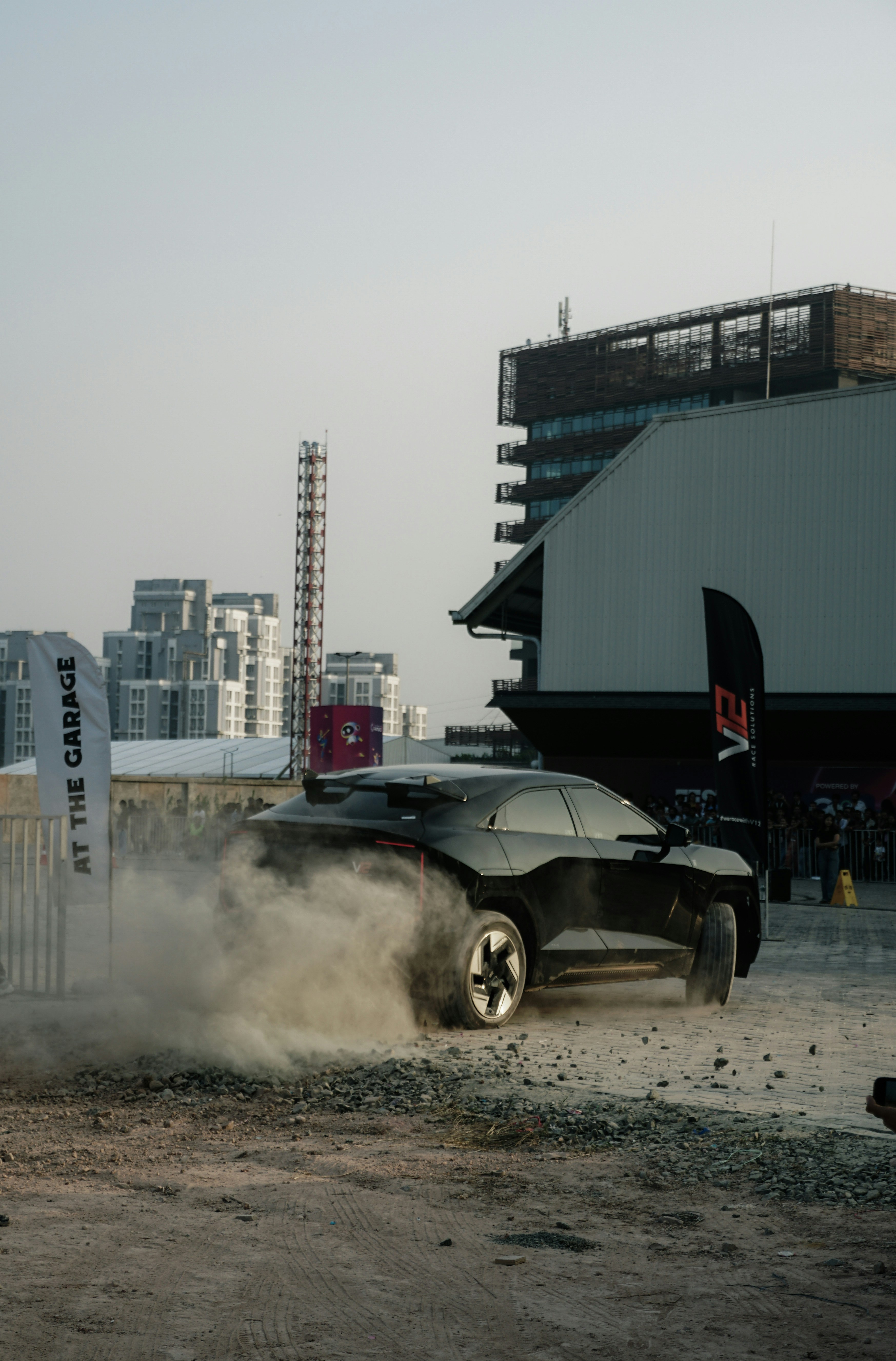A black car kicks up dust while turning