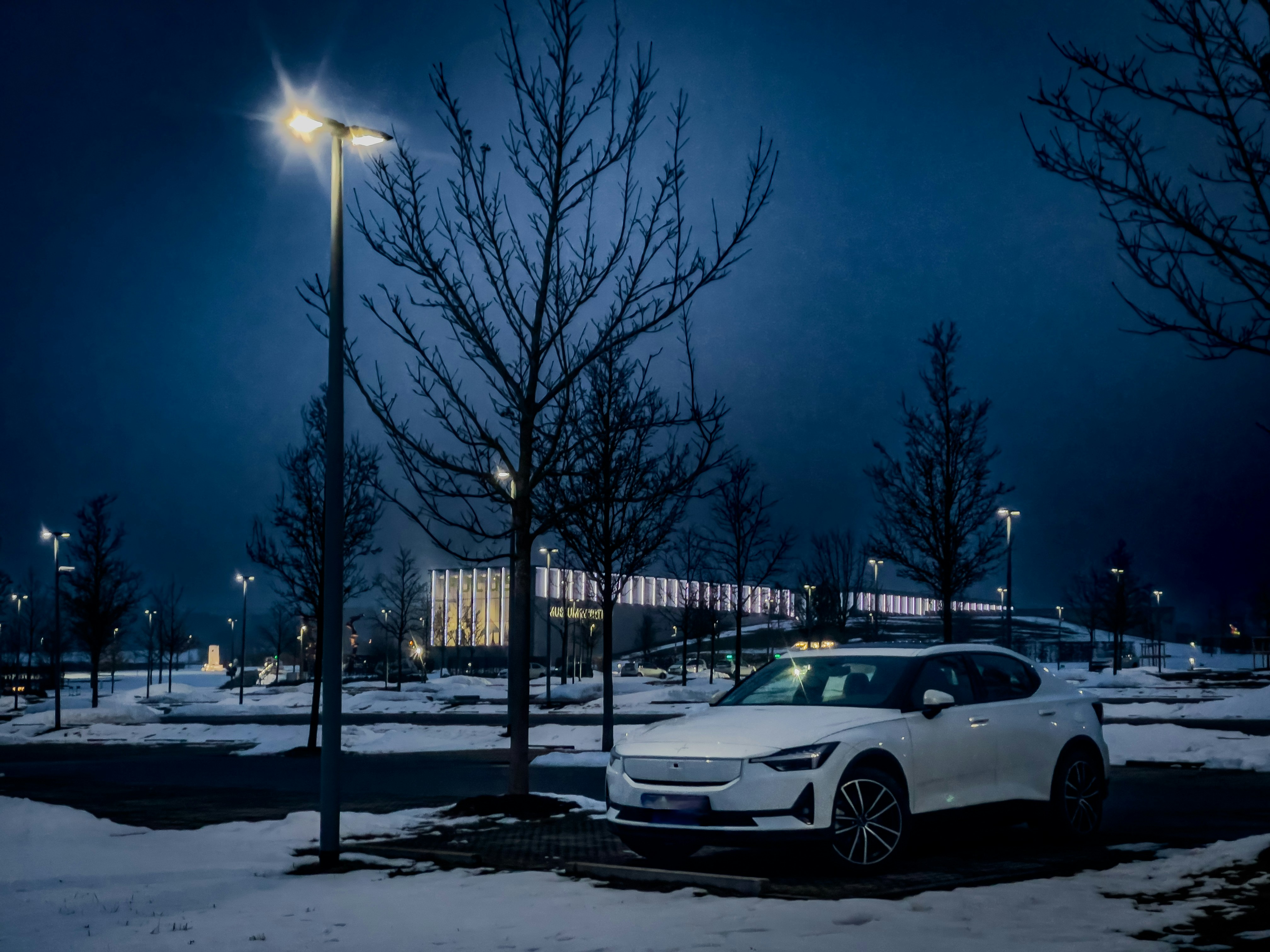 White car parked in a snowy lot at night.
