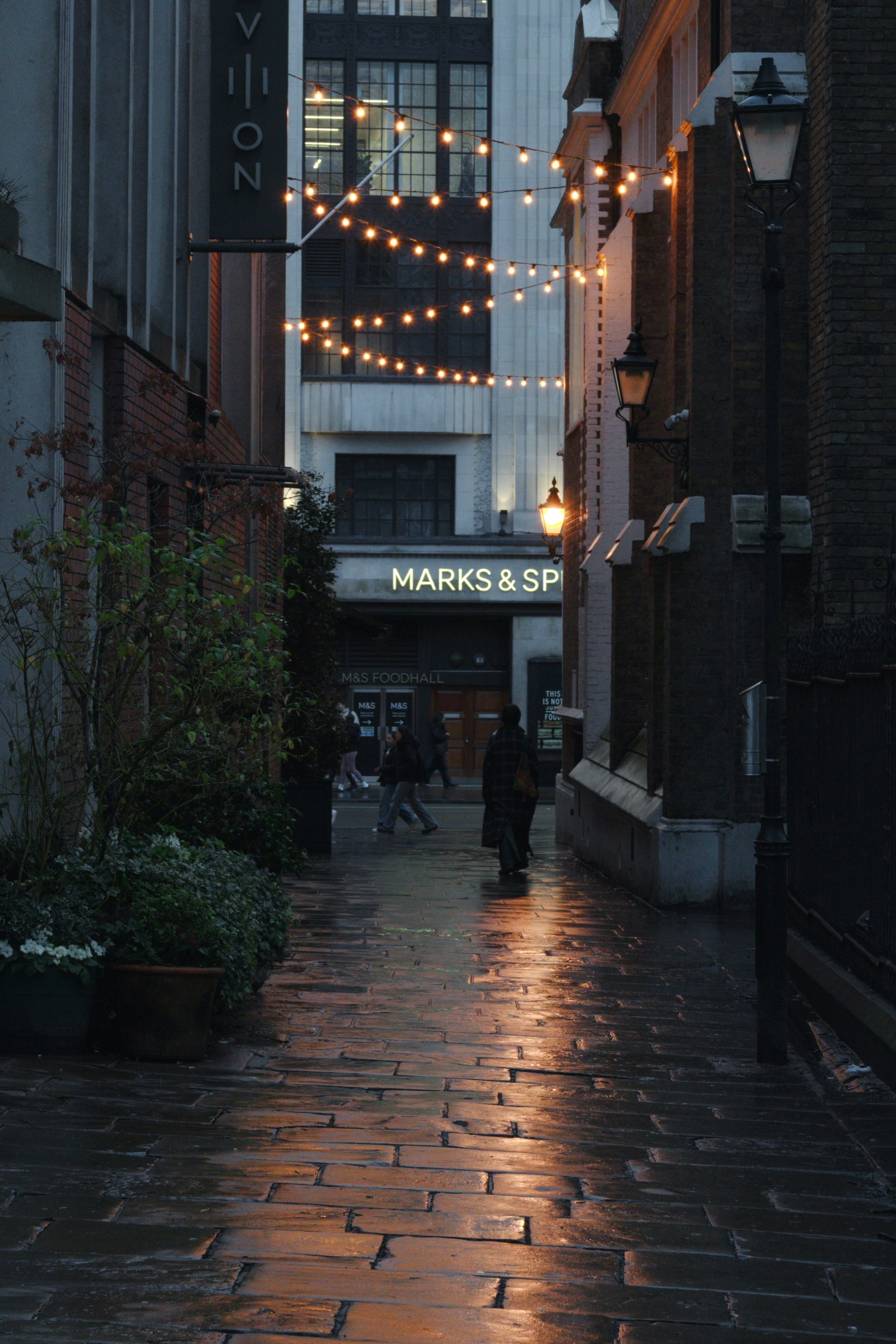 Rainy alleyway with string lights reflecting on wet cobblestones