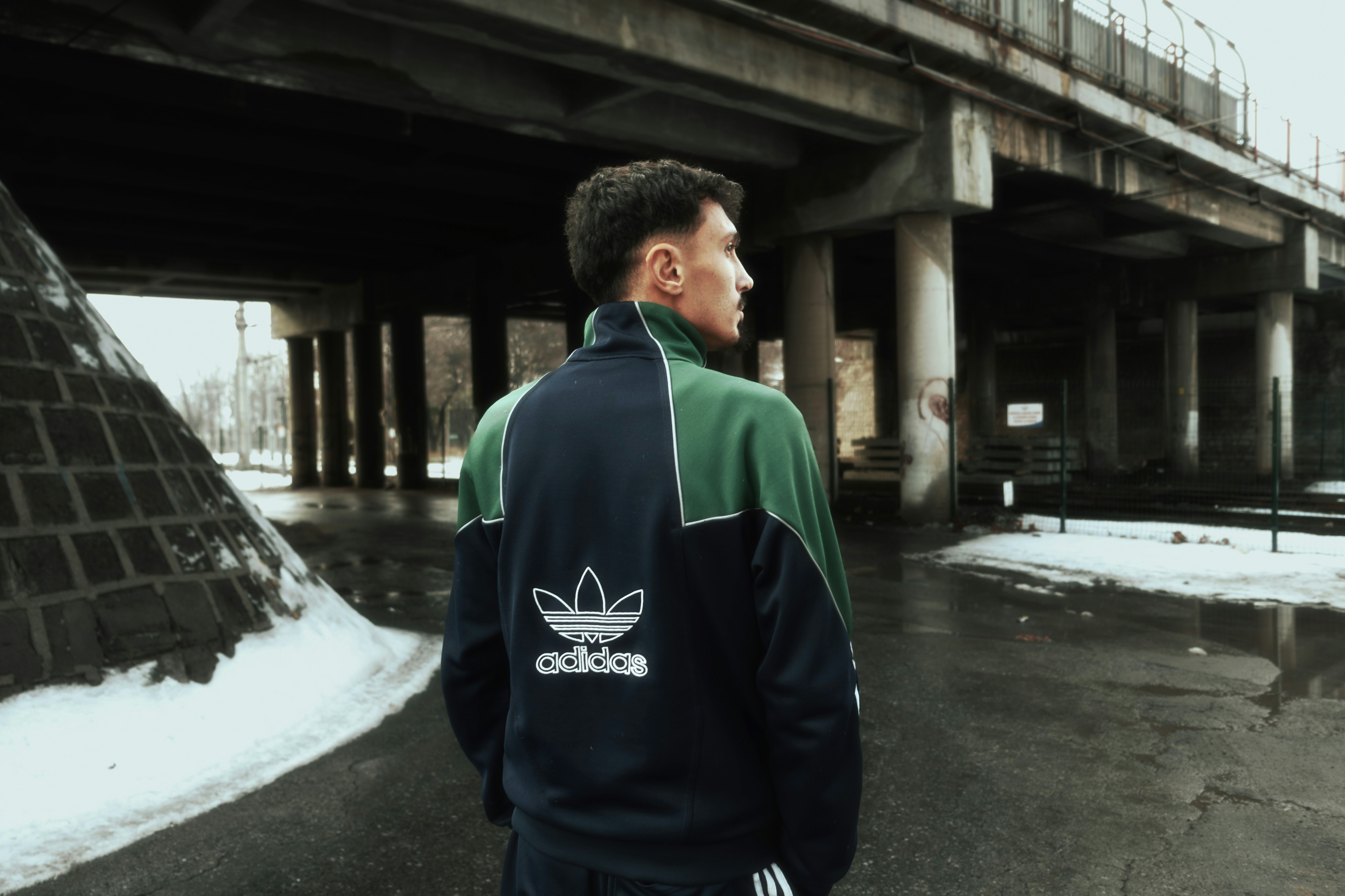 Man wearing adidas jacket under a bridge