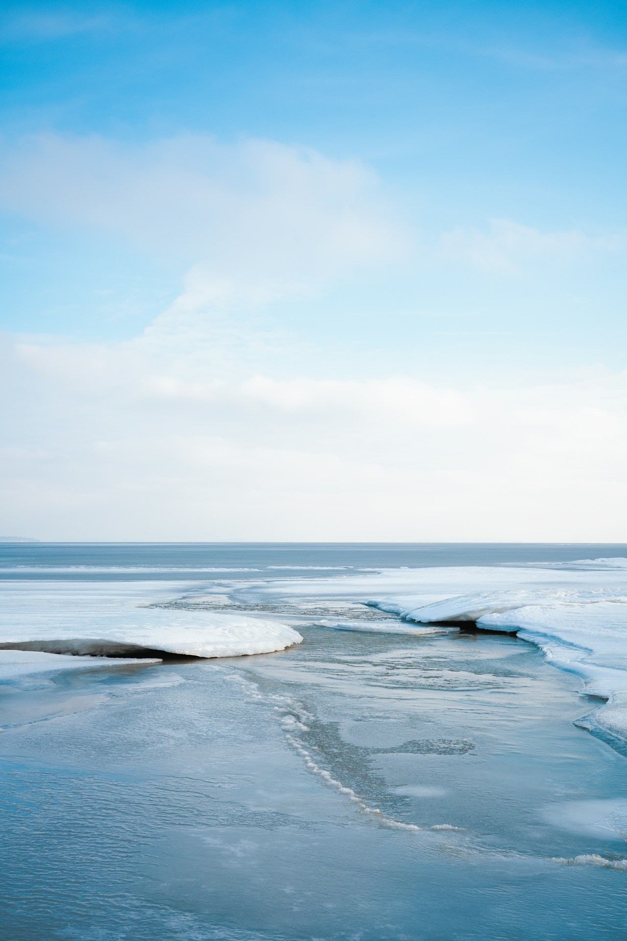 An open water lane running between ice sheets on a frozen sea under a pale blue sky
