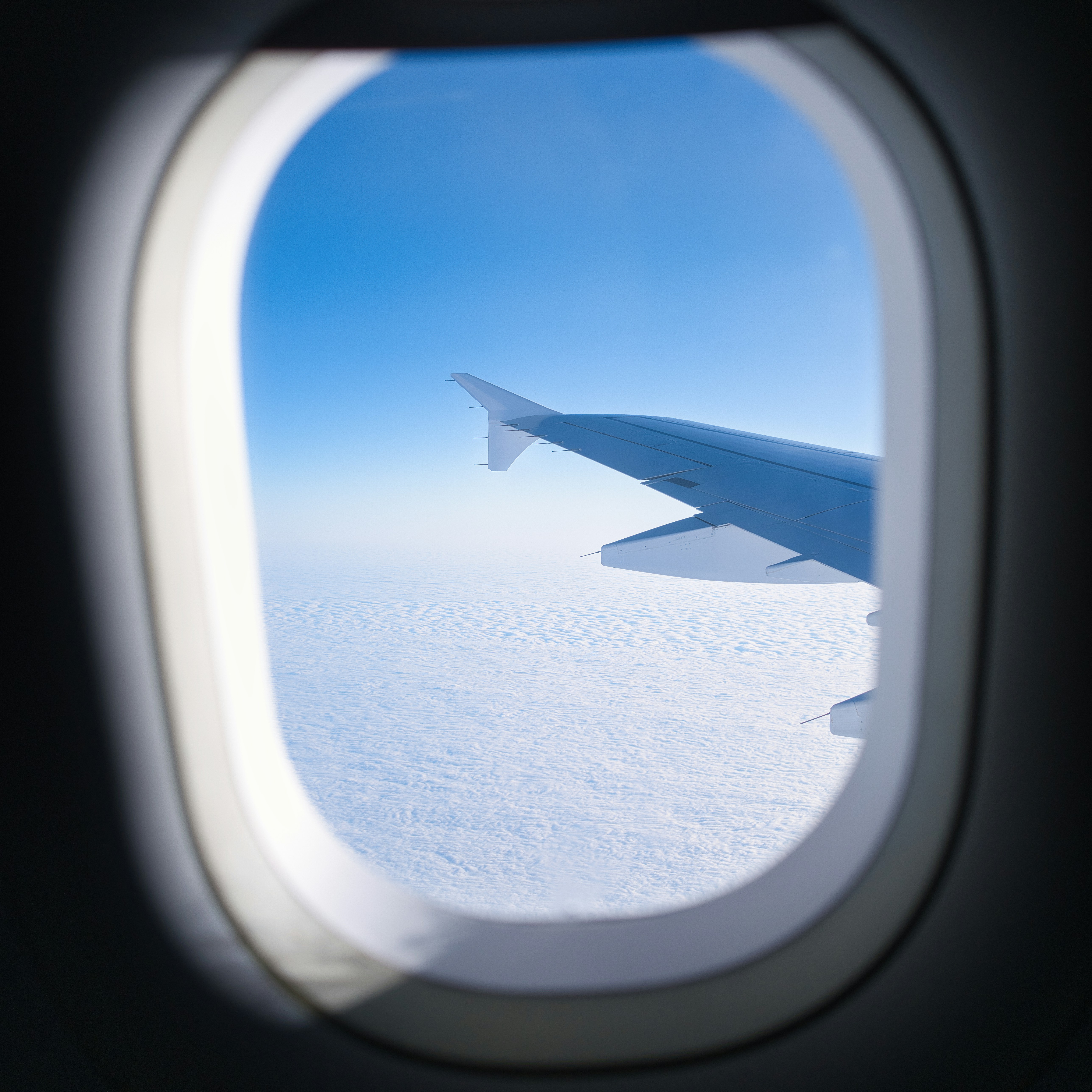 Airplane wing seen through window above clouds