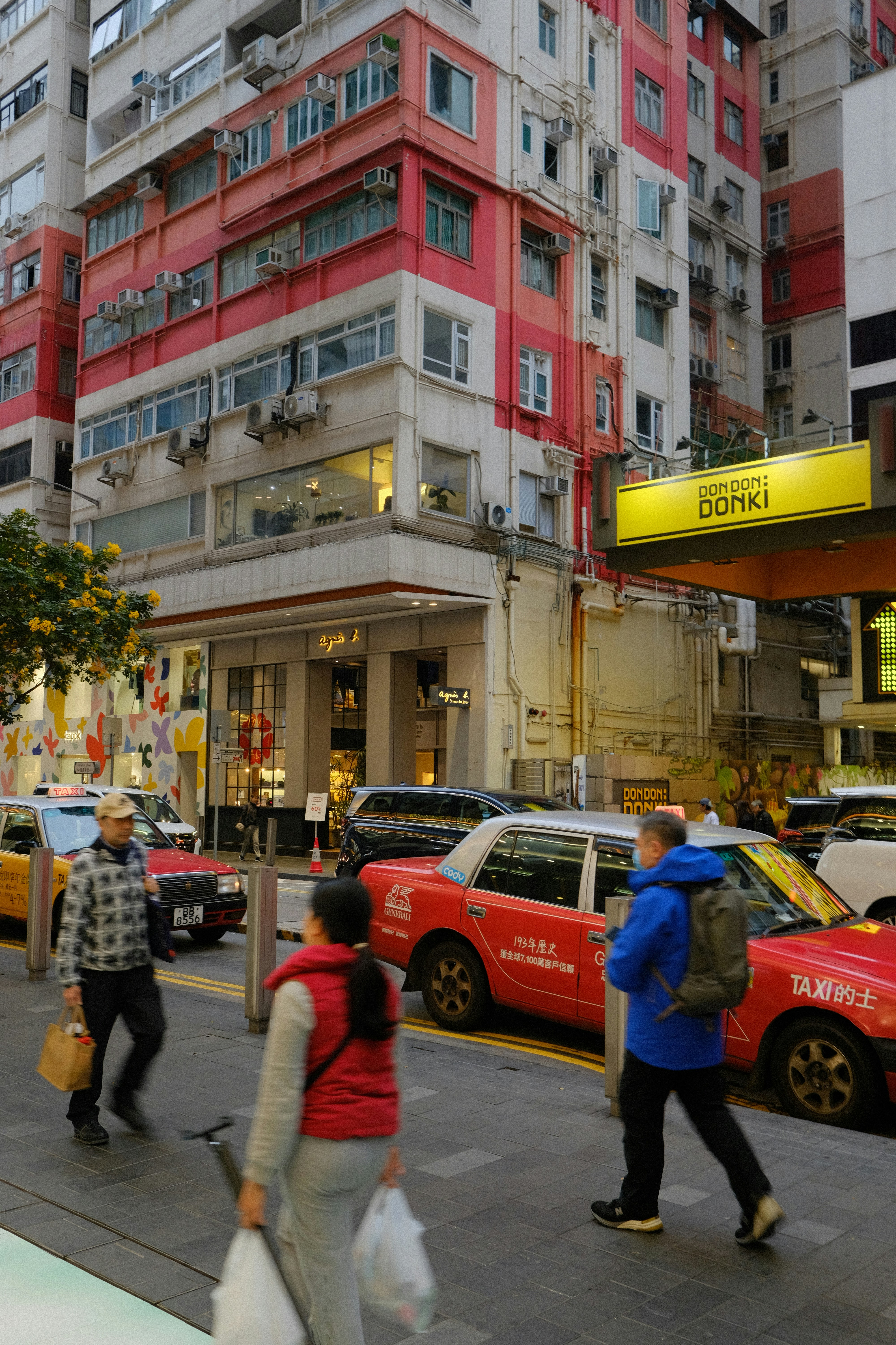 People walk past red taxis on a city street.