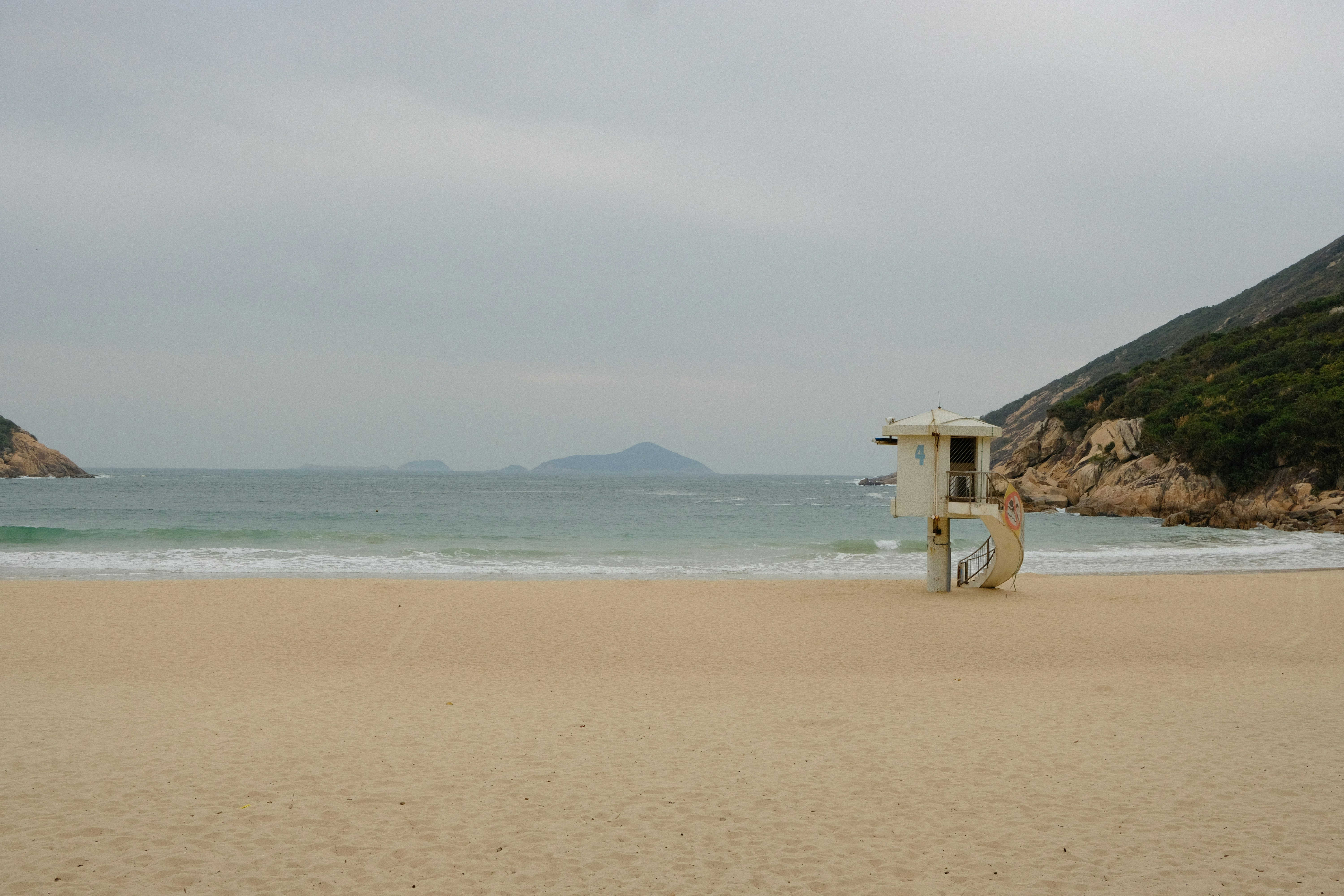 Lifeguard tower on a sandy beach with ocean waves.