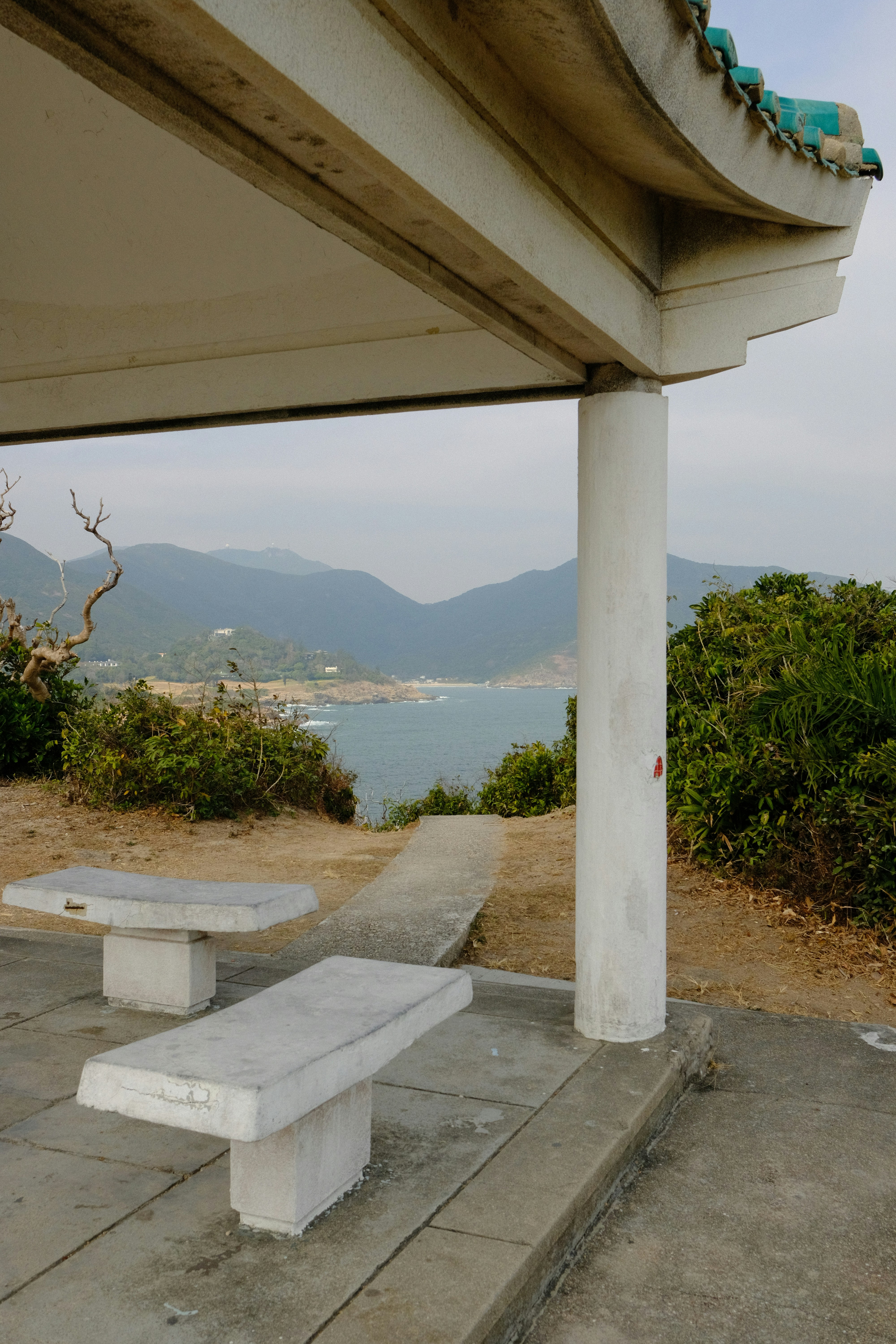 Two stone benches under a pavilion overlooking the sea.