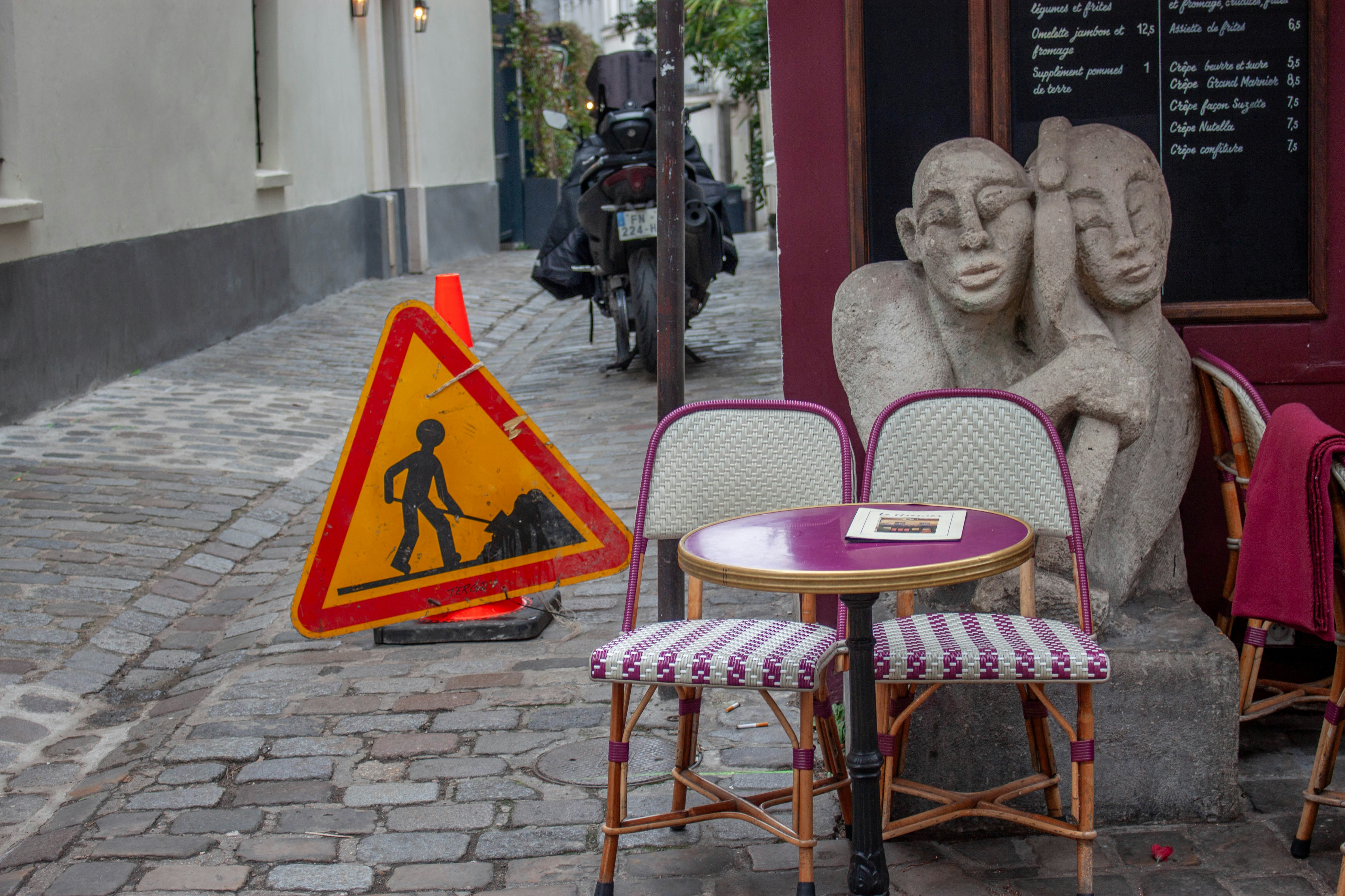 Outdoor cafe seating with construction sign and sculpture.
