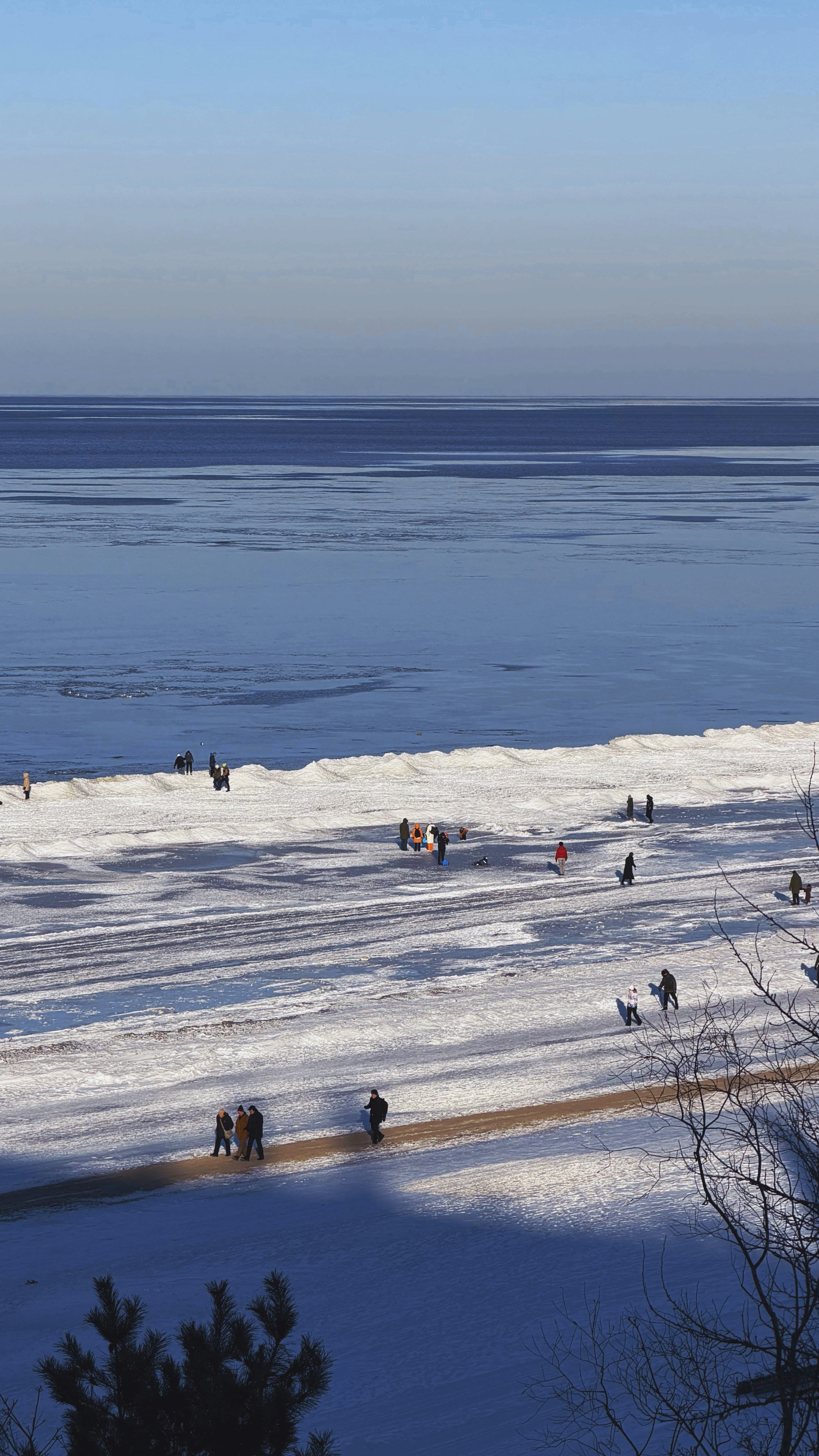 凍った海のそばの雪に覆われた浜辺を歩く人々。