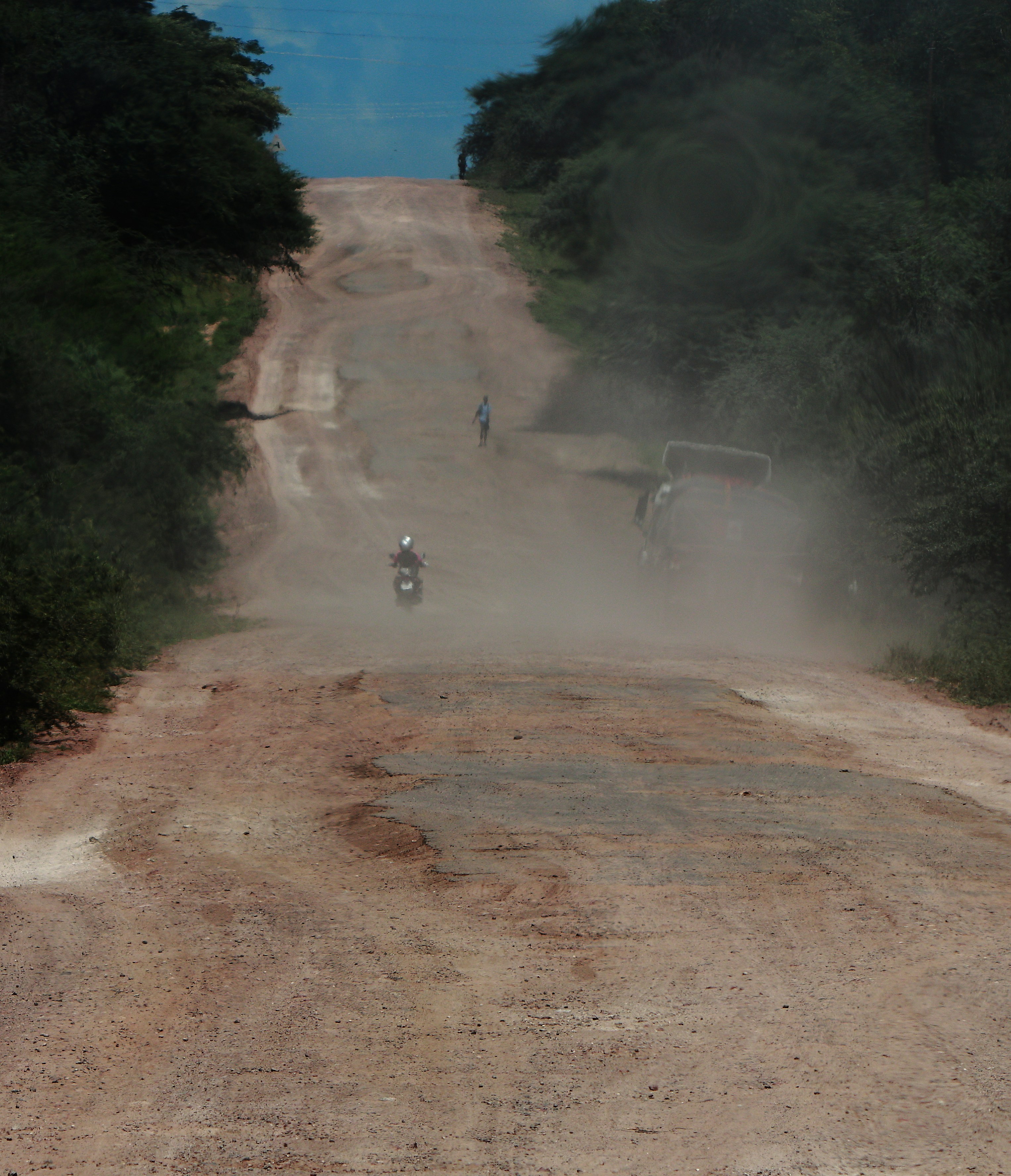 Dusty dirt road with vehicles and trees