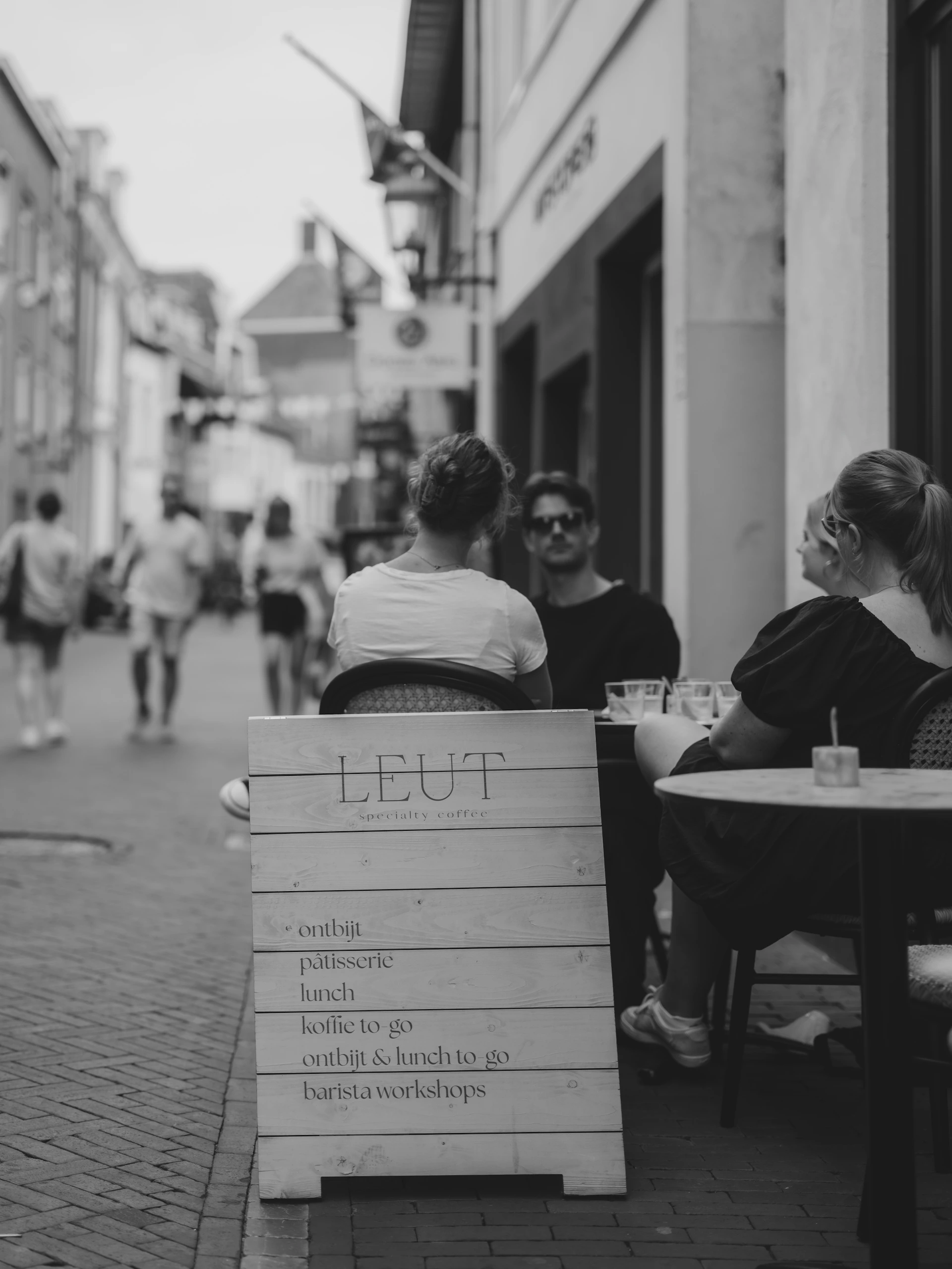 People sitting at tables outside a cafe with menu board