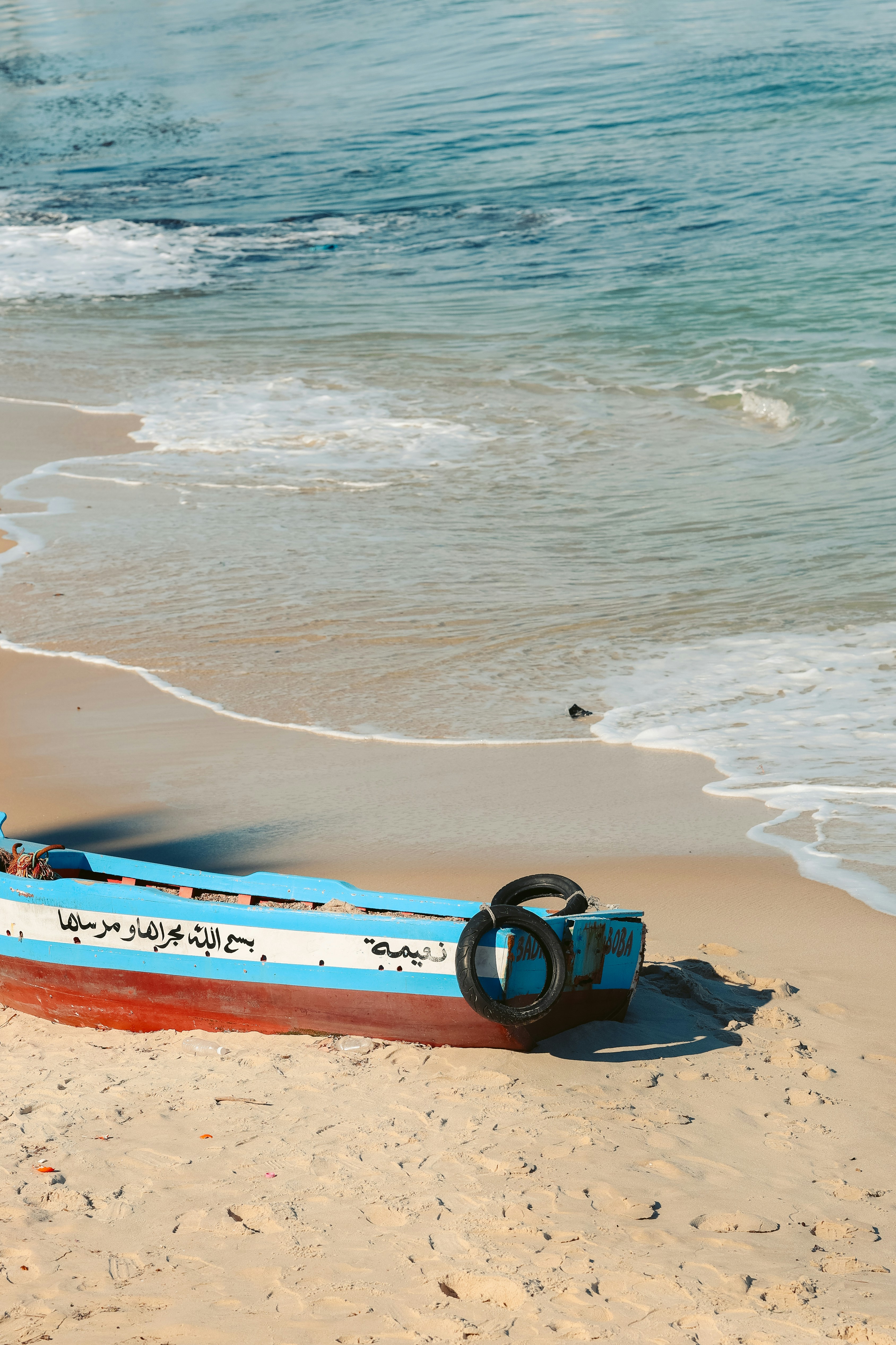 Ein blau-rotes Boot liegt an einem Sandstrand.