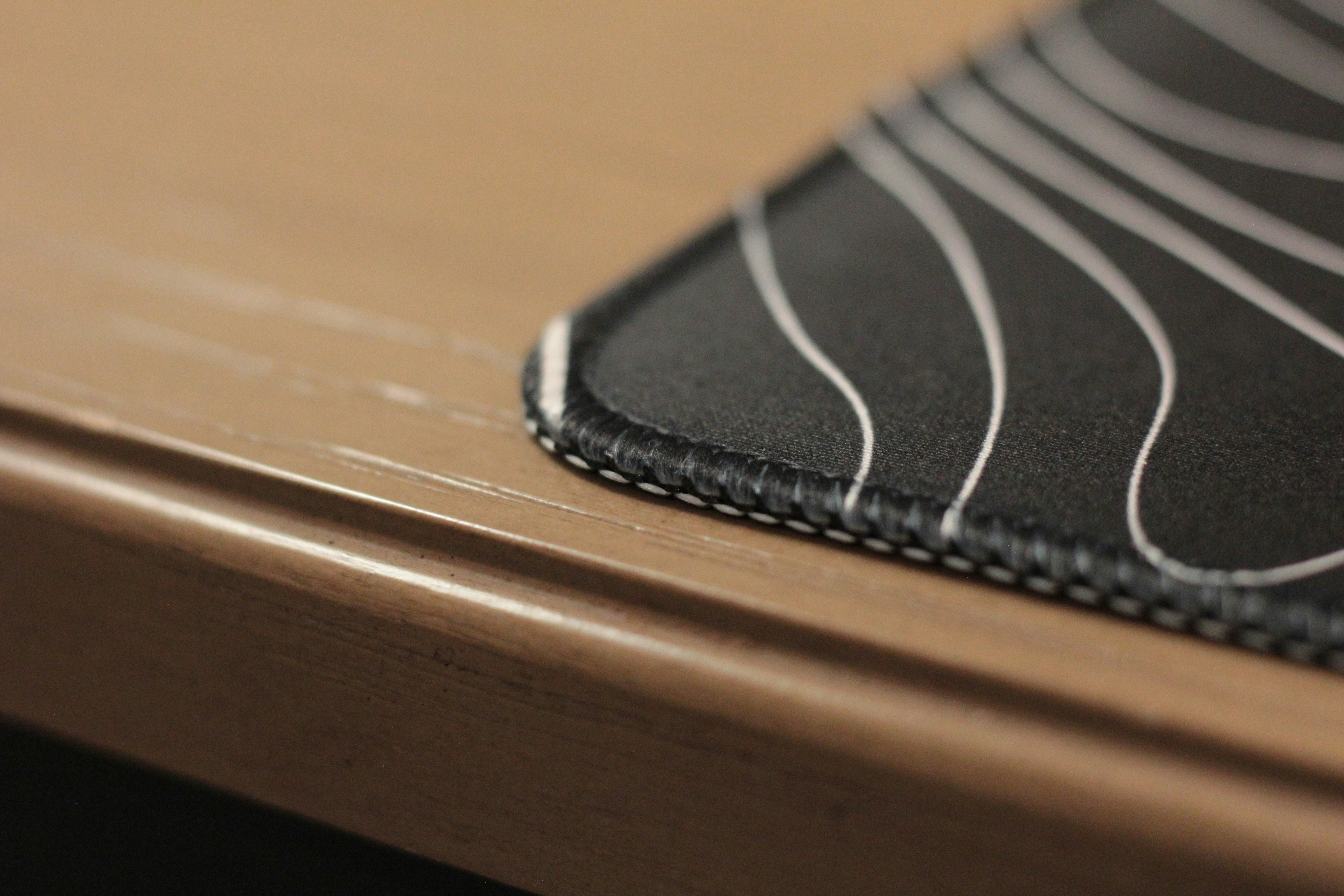 Close-up of a black mousepad on a wooden desk.