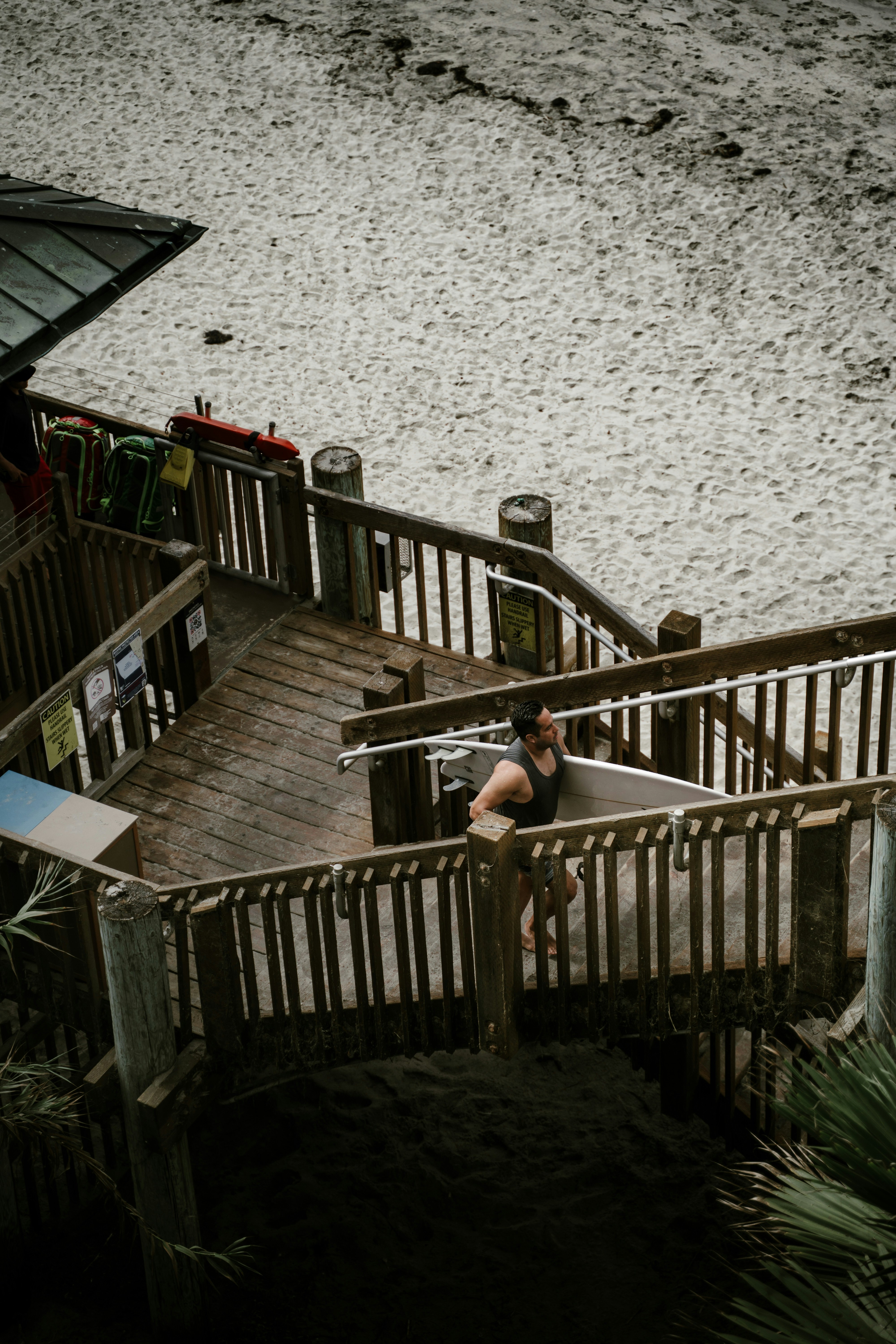Woman carrying surfboard up wooden beach stairs