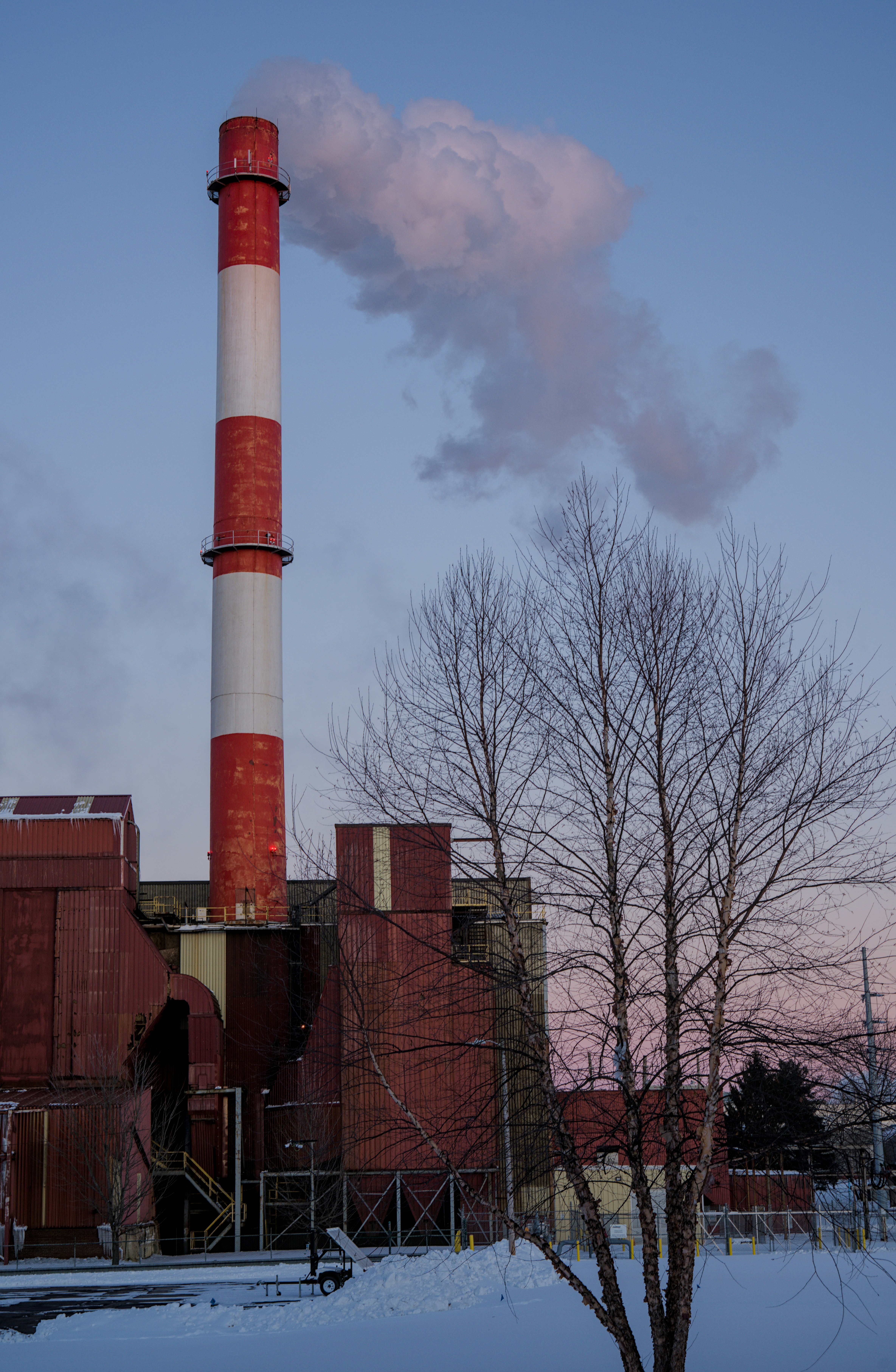 Red and white smokestack emitting smoke against sky
