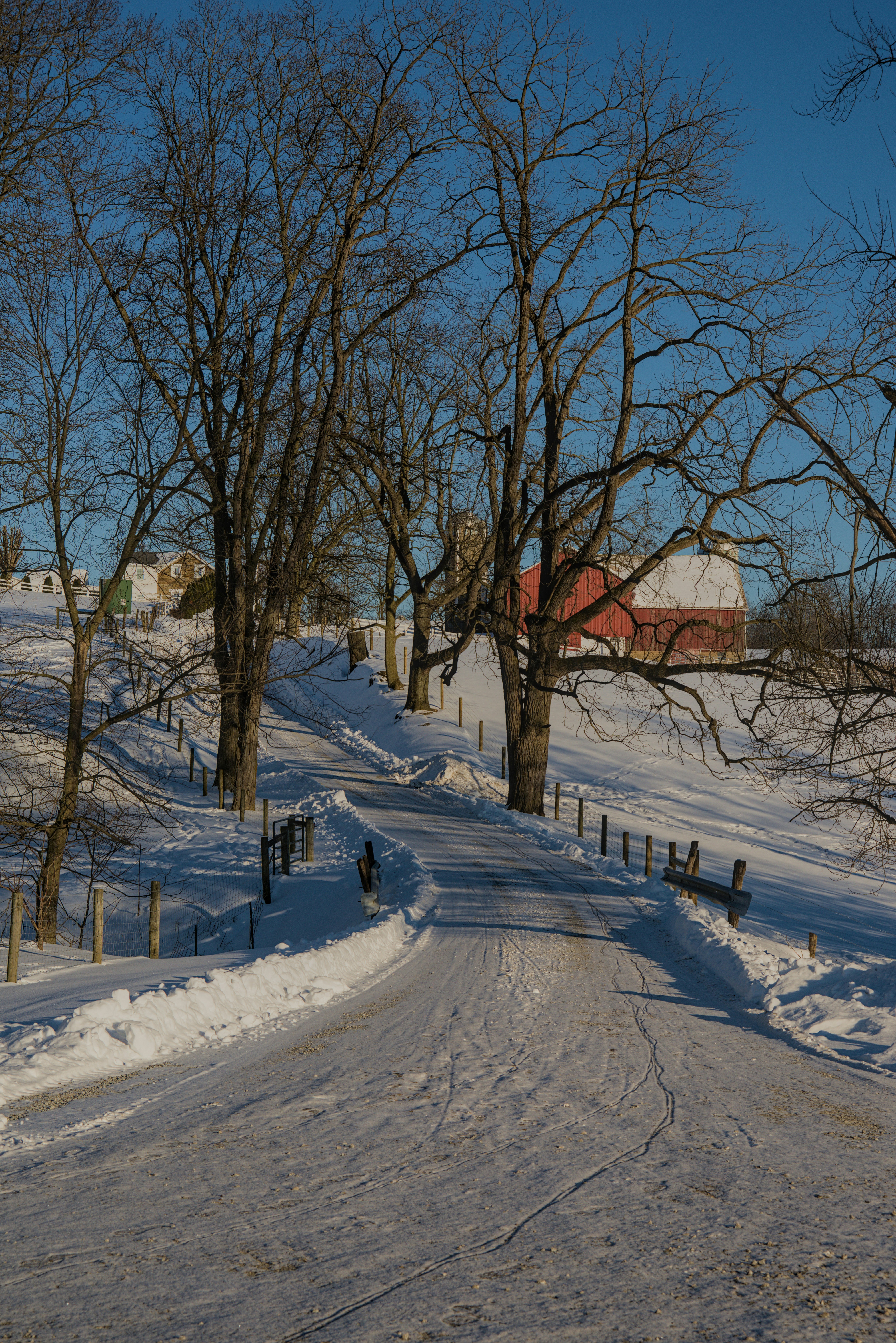 Snowy road leads to a red barn in winter.